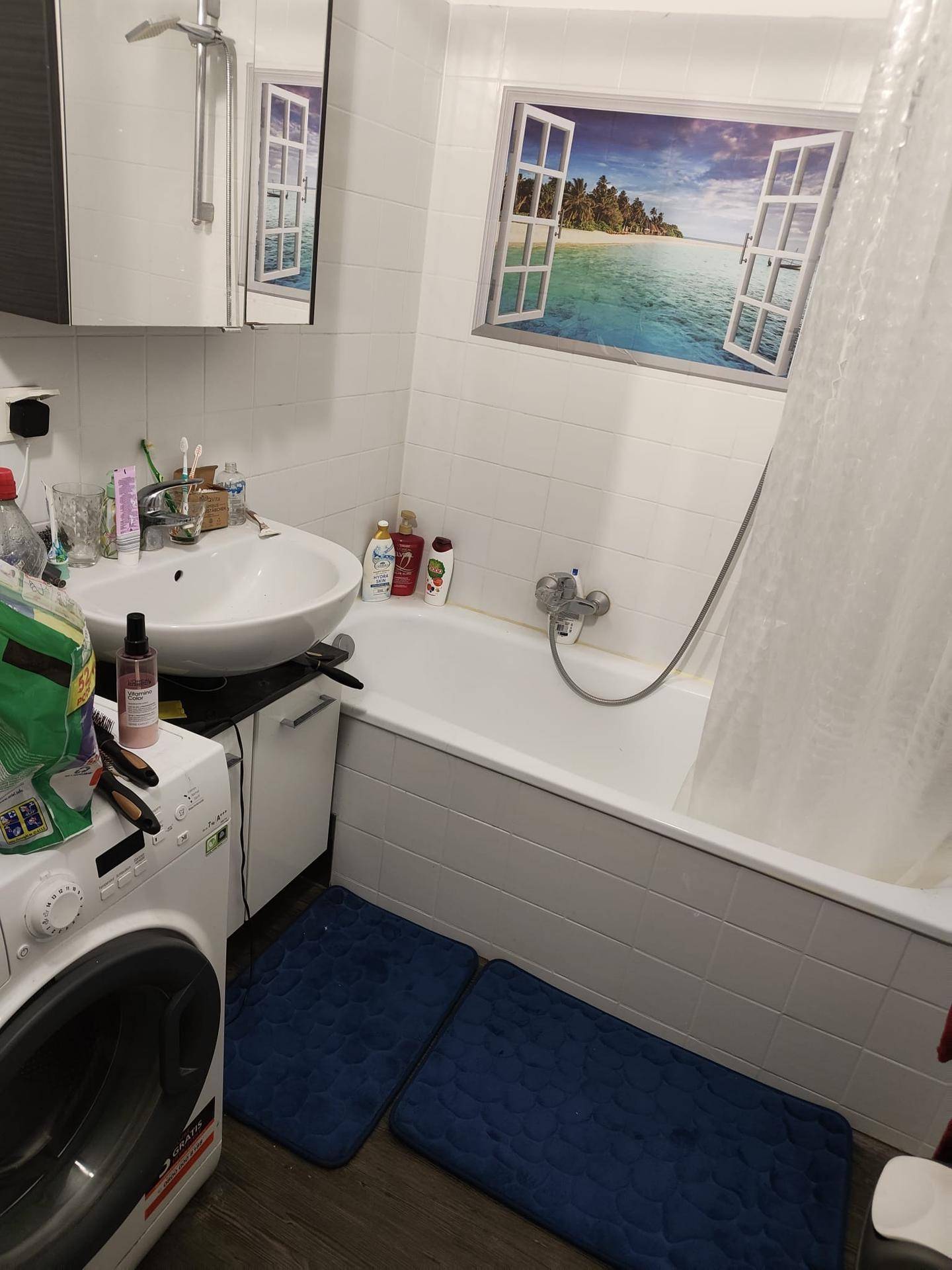 Helles Badezimmer mit Badewanne, Waschbecken und Waschmaschine, komplett gefliest.