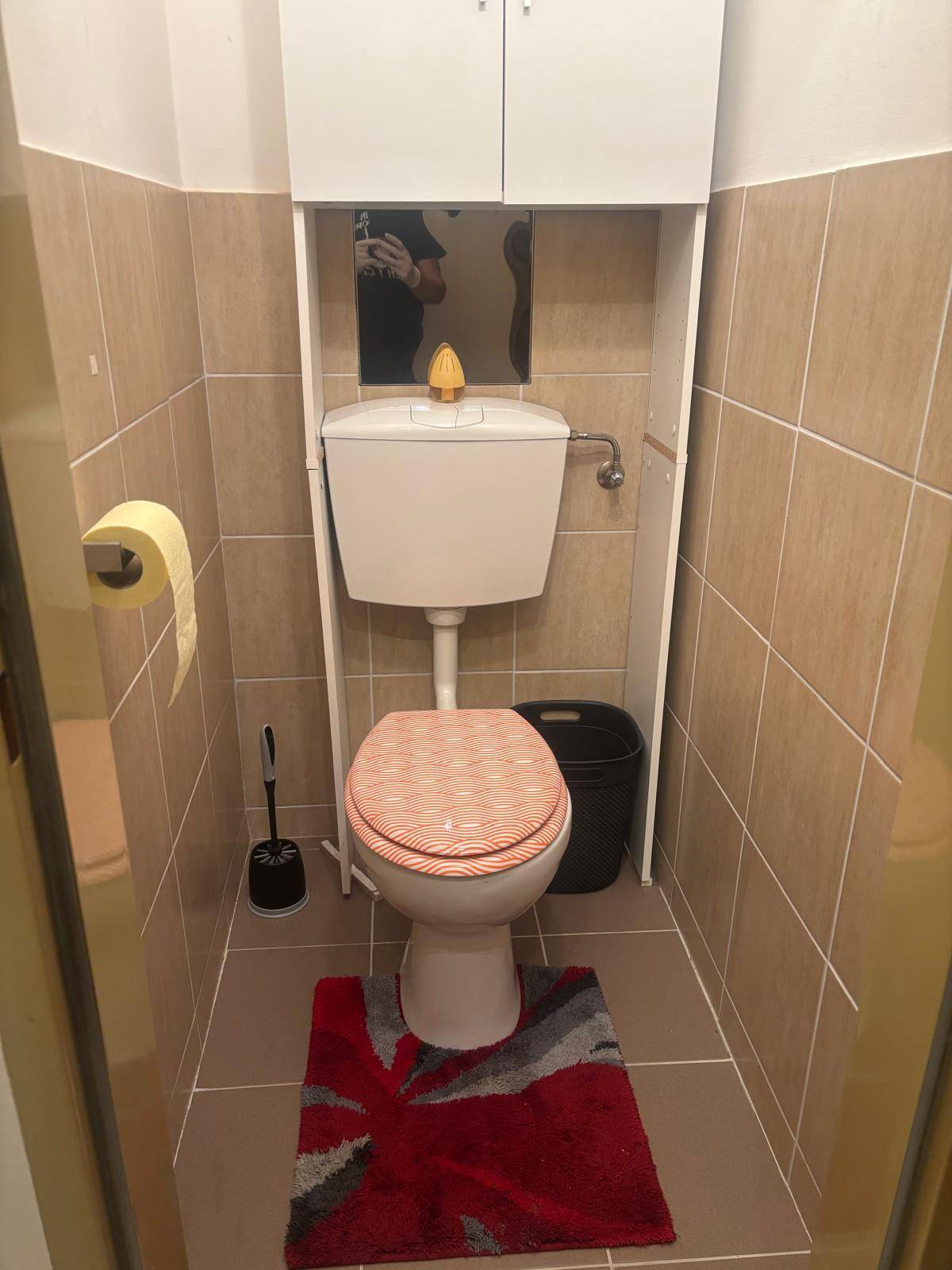 Kleines Gäste-WC mit beigefarbenen Wand- und Bodenfliesen und einem Spülkasten.