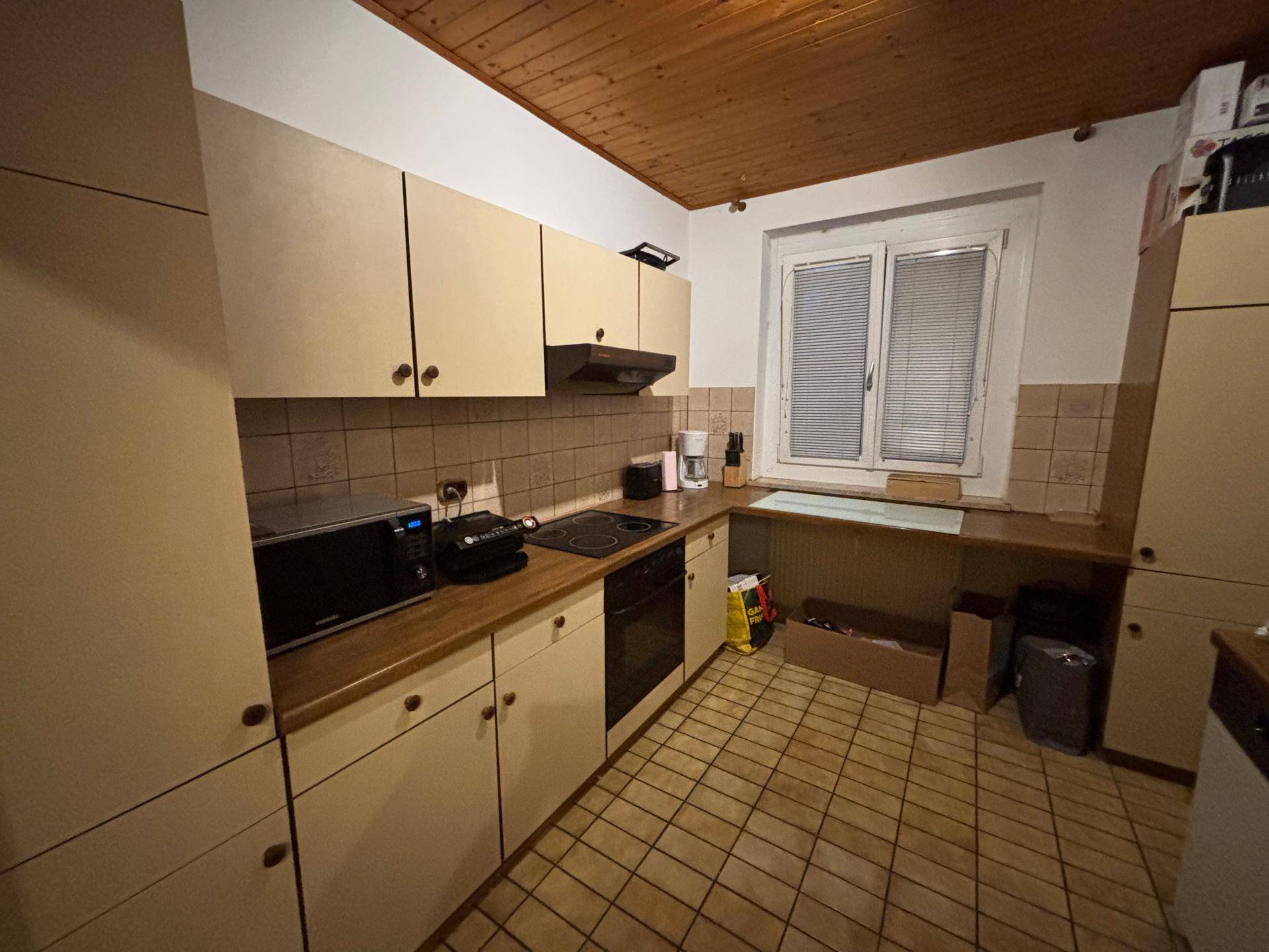 Funktionale Küche mit beigefarbenen Schränken, Holz-Arbeitsplatte und Fenster für Tageslicht.