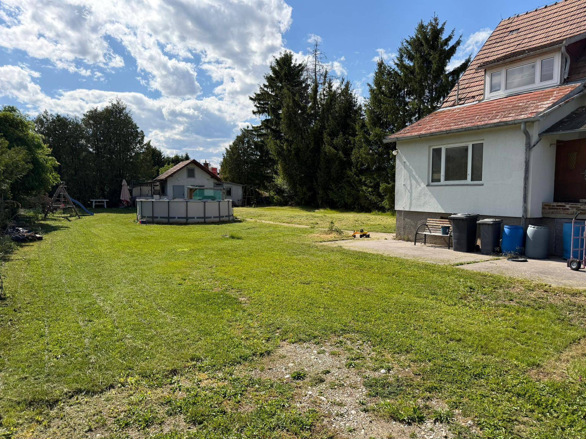 Großer Gartenbereich mit Rasenfläche, Aufstellpool und Spielgeräten unter blauem Himmel.