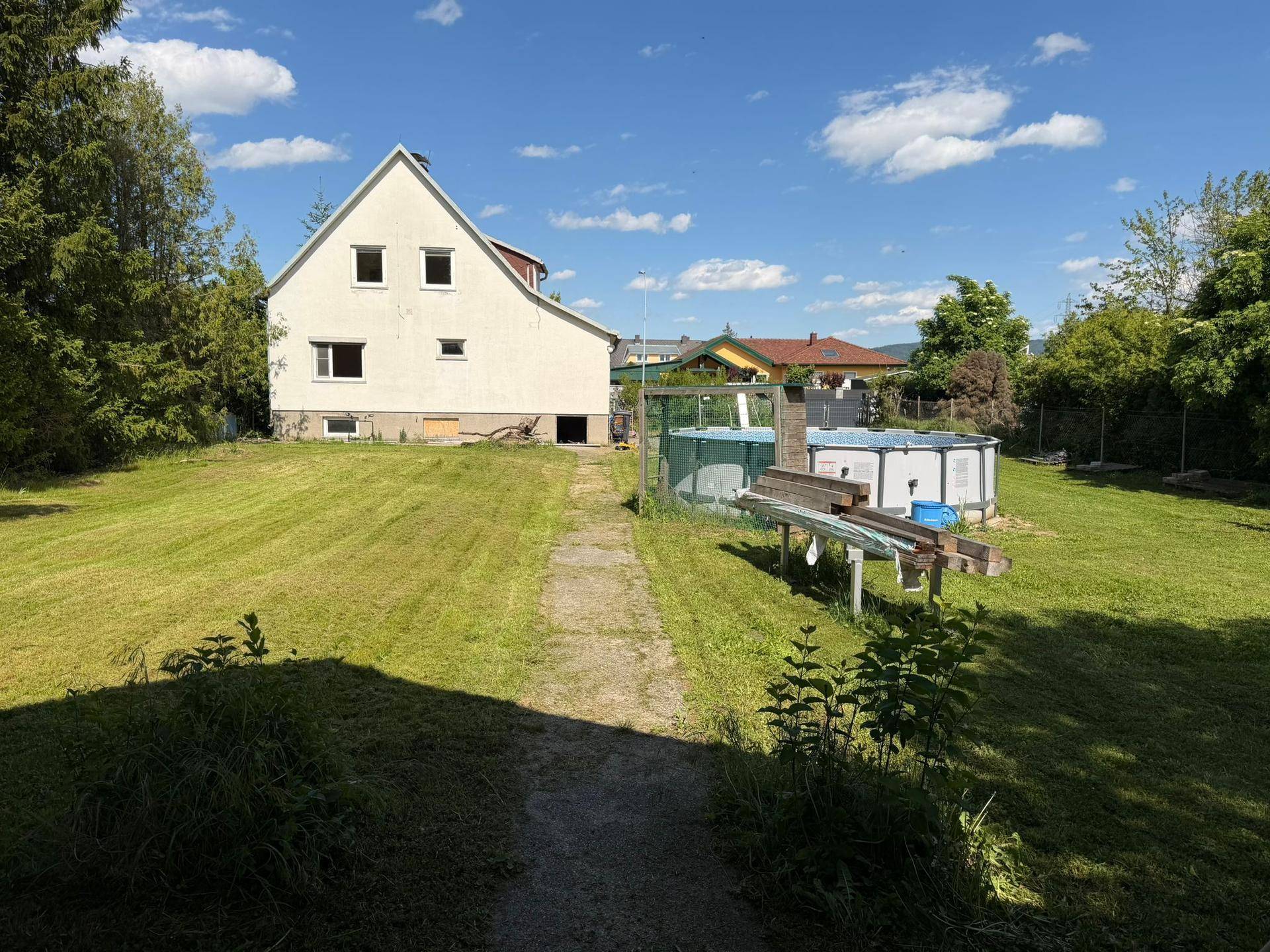 Hinteransicht des Hauses mit großem Garten, Aufstellpool und viel Grünfläche an einem sonnigen Tag.