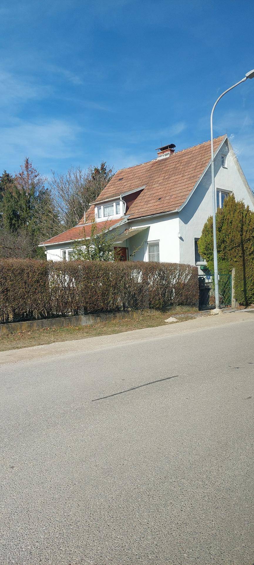 Einfamilienhaus mit Ziegeldach und Hecke vom Straßenrand aus gesehen an einem sonnigen Tag.