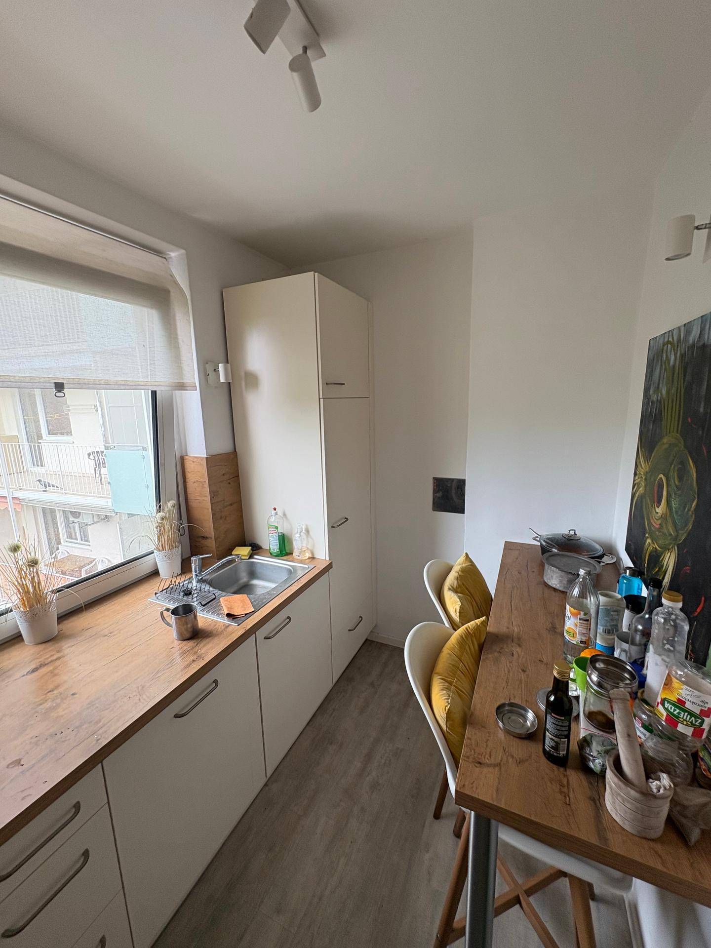 Schmale Küche mit Essbereich, weißen Schränken und einem Fenster mit Blick auf die Nachbarschaft.