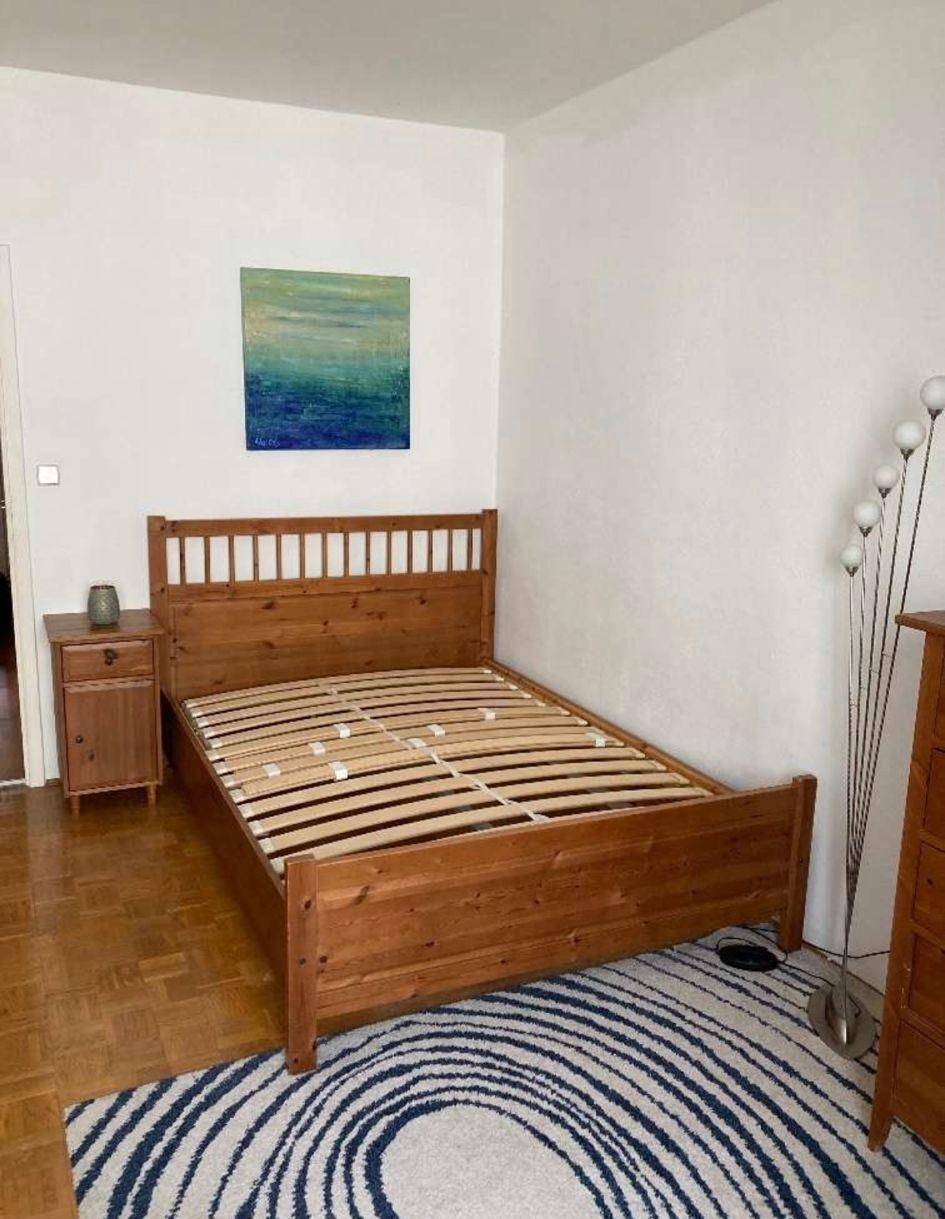 Helles Schlafzimmer mit Holzbett, Nachttisch und einem abstrakten Kunstwerk an der Wand.