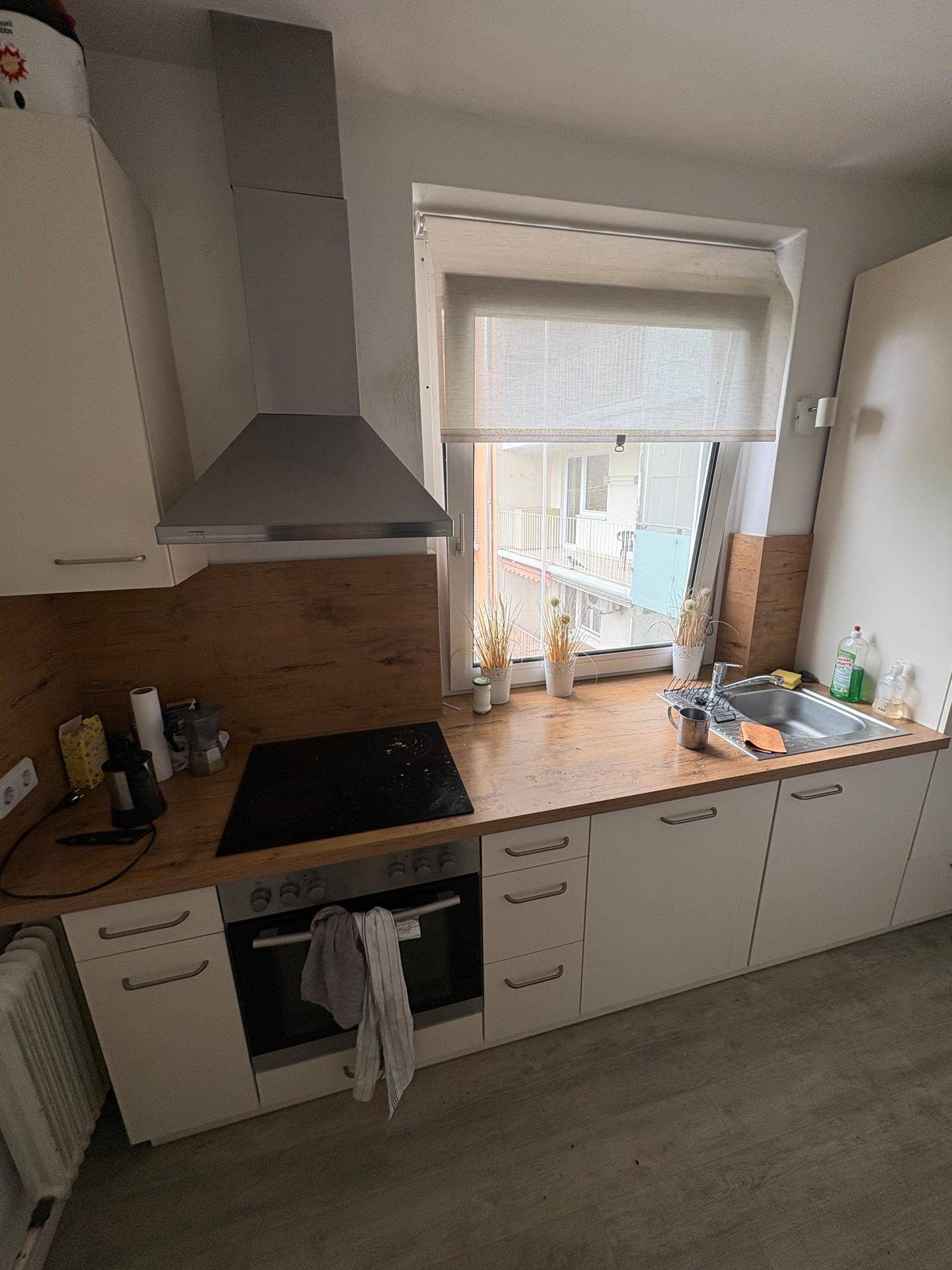 Moderne Küche mit weißen Unterschränken, Holzarbeitsplatte, Induktionskochfeld und Dunstabzugshaube.