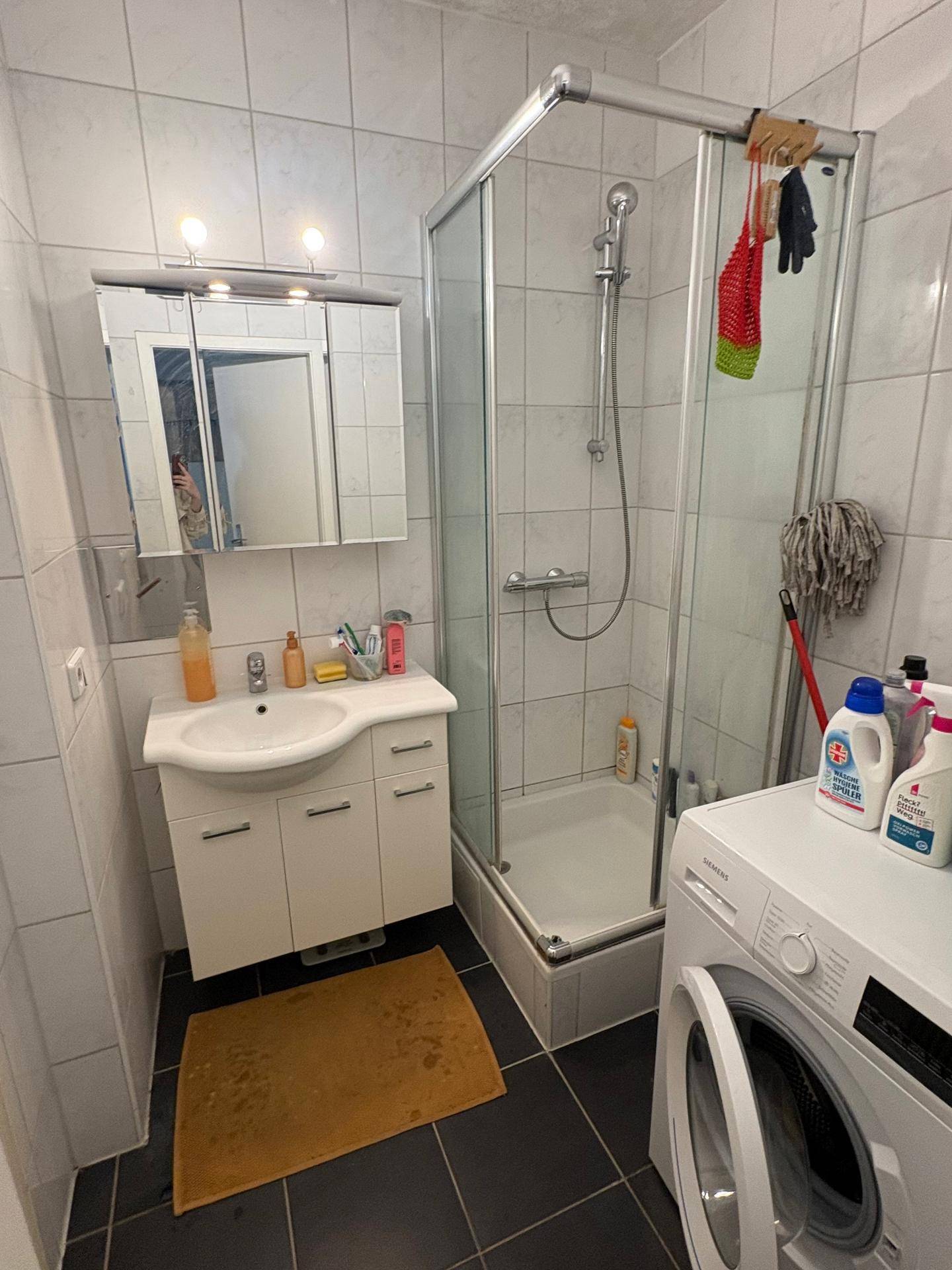 Badezimmer mit Duschkabine, Waschbeckenunterschrank, Spiegelschrank und Waschmaschine.