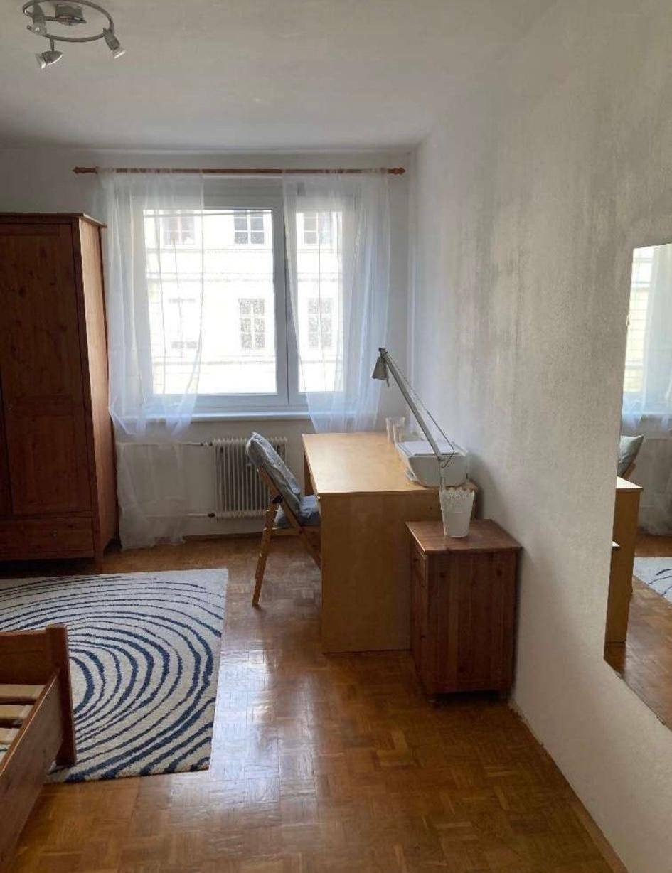 Schlafzimmer mit Schreibtisch, Stuhl und einem großen Fenster, das viel Tageslicht hereinlässt.