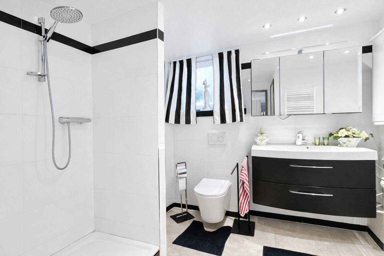 Modernes Badezimmer mit Dusche, schwarzen Akzenten und Spiegelschrank über dem Waschtisch.