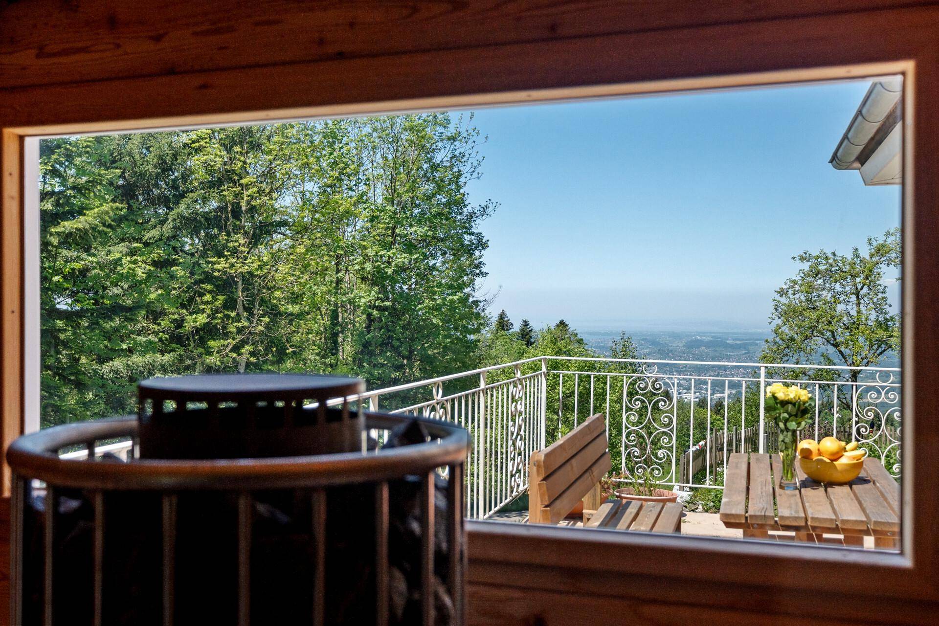 Blick aus der Fasssauna auf den Balkon mit Sitzgelegenheiten und weitem Ausblick.