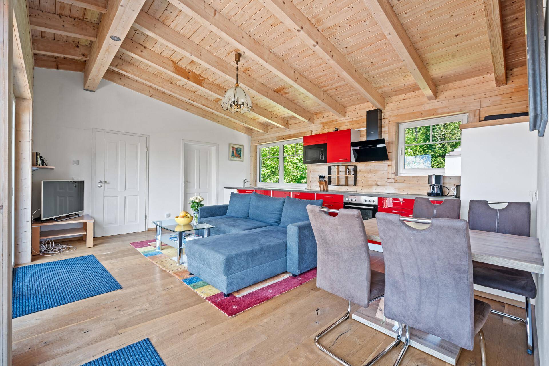 Offener Wohn-Essbereich mit roter Küche, blauem Sofa und Holzbalkendecke.