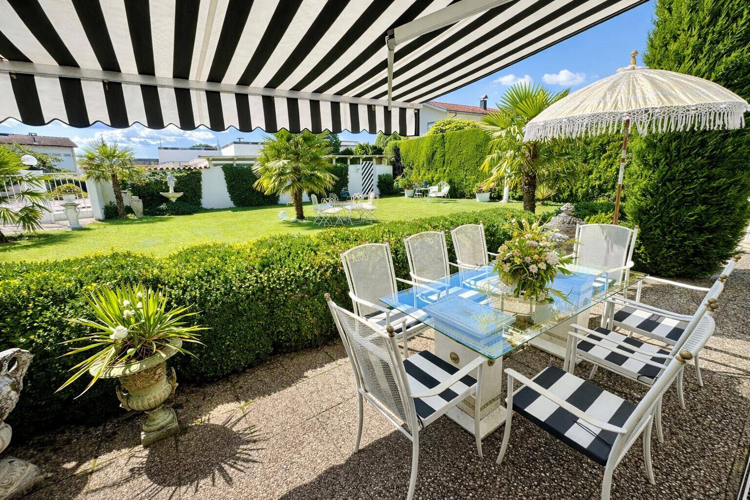 Sonnige Terrasse mit gestreifter Markise, Esstisch und Blick auf den üppigen Garten.