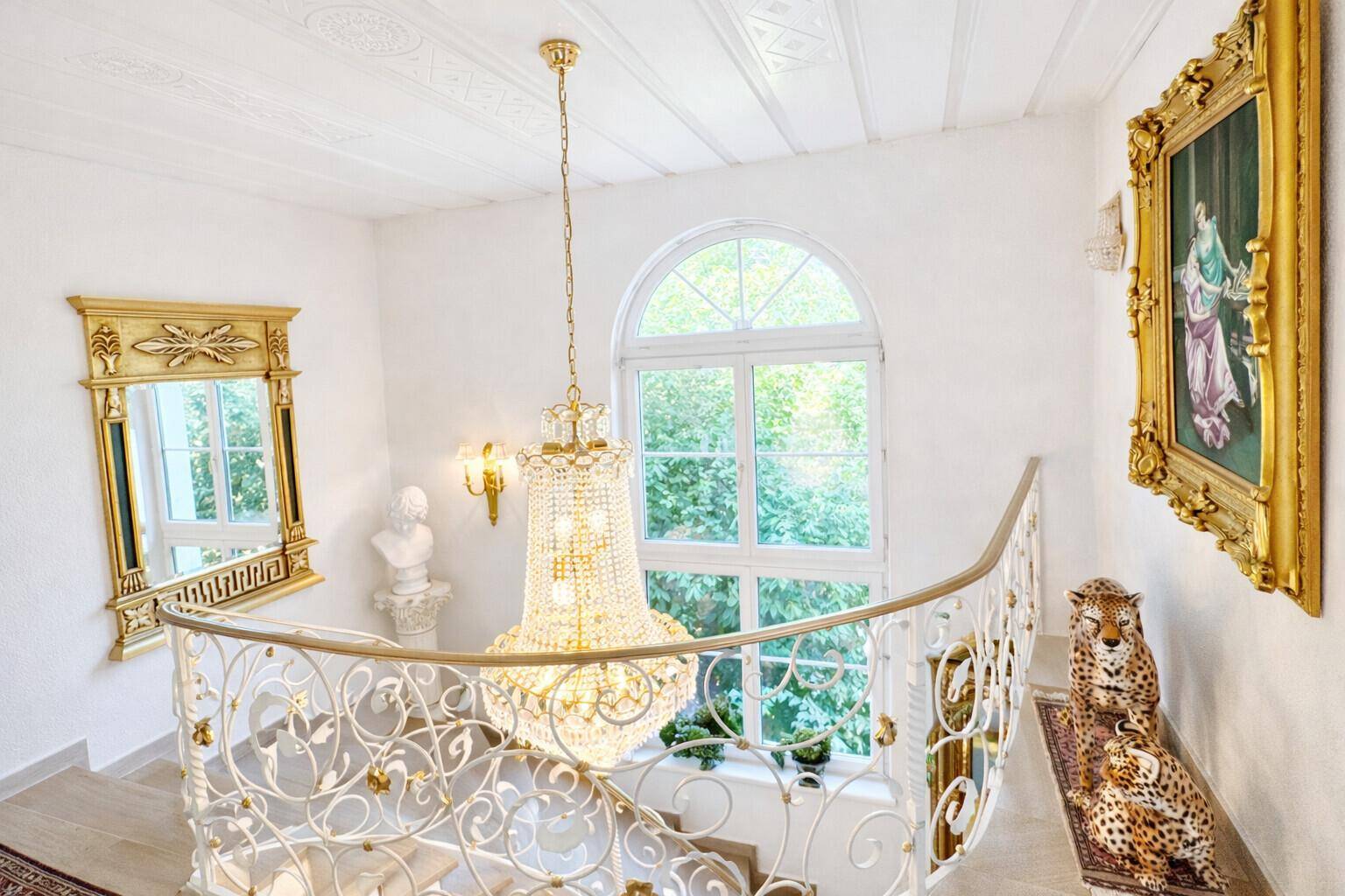 Geschwungene Treppe mit schmiedeeisernem Geländer und großem Bogenfenster, das viel Licht hereinlässt.