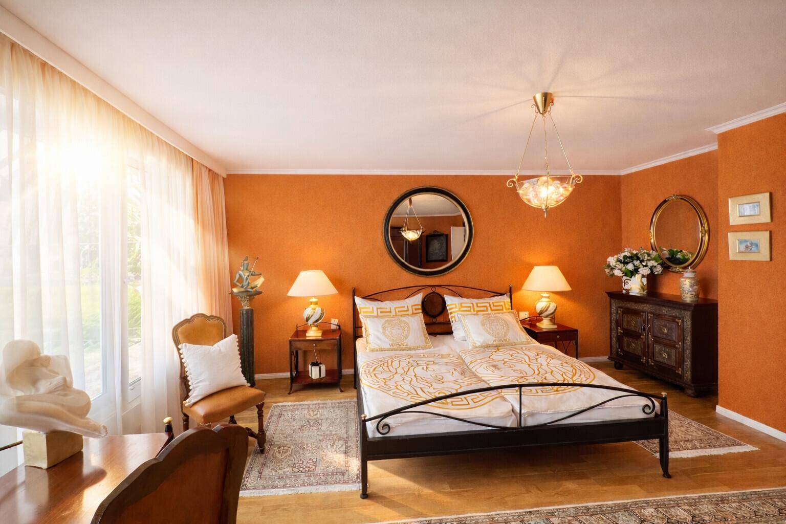 Sonniges Schlafzimmer mit orangefarbenen Wänden, großem Fenster und klassischem Doppelbett.