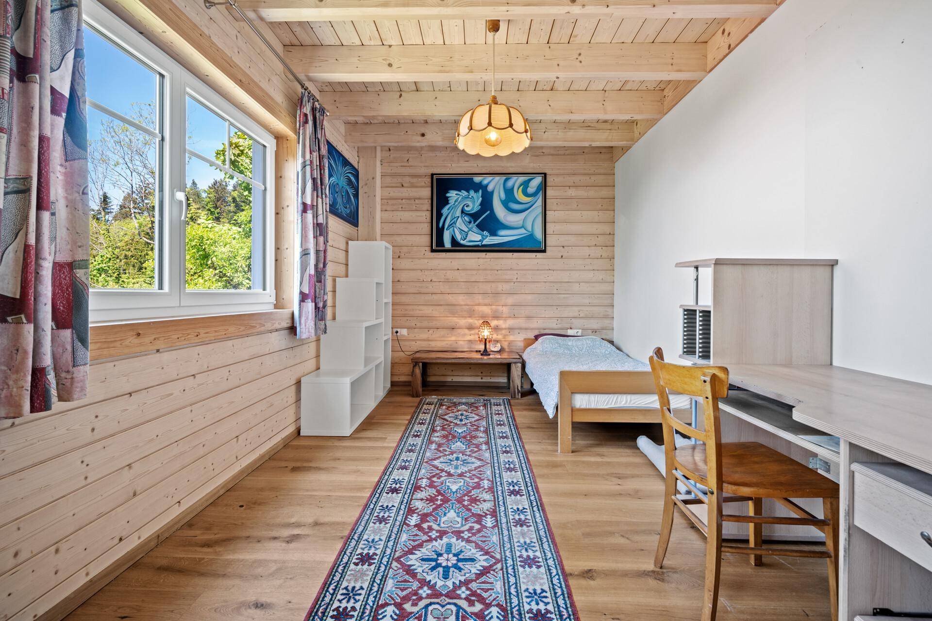 Helles Schlafzimmer mit Einzelbett, Schreibtisch, Holzboden und Holzwänden.