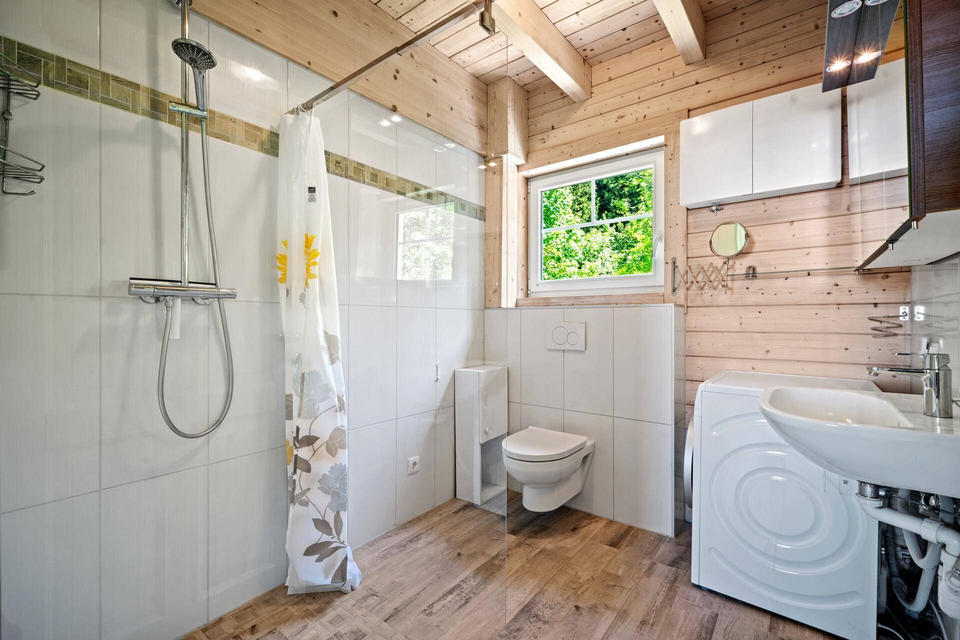 Funktionales Badezimmer mit Dusche, Toilette, Waschmaschine und Holzwänden.