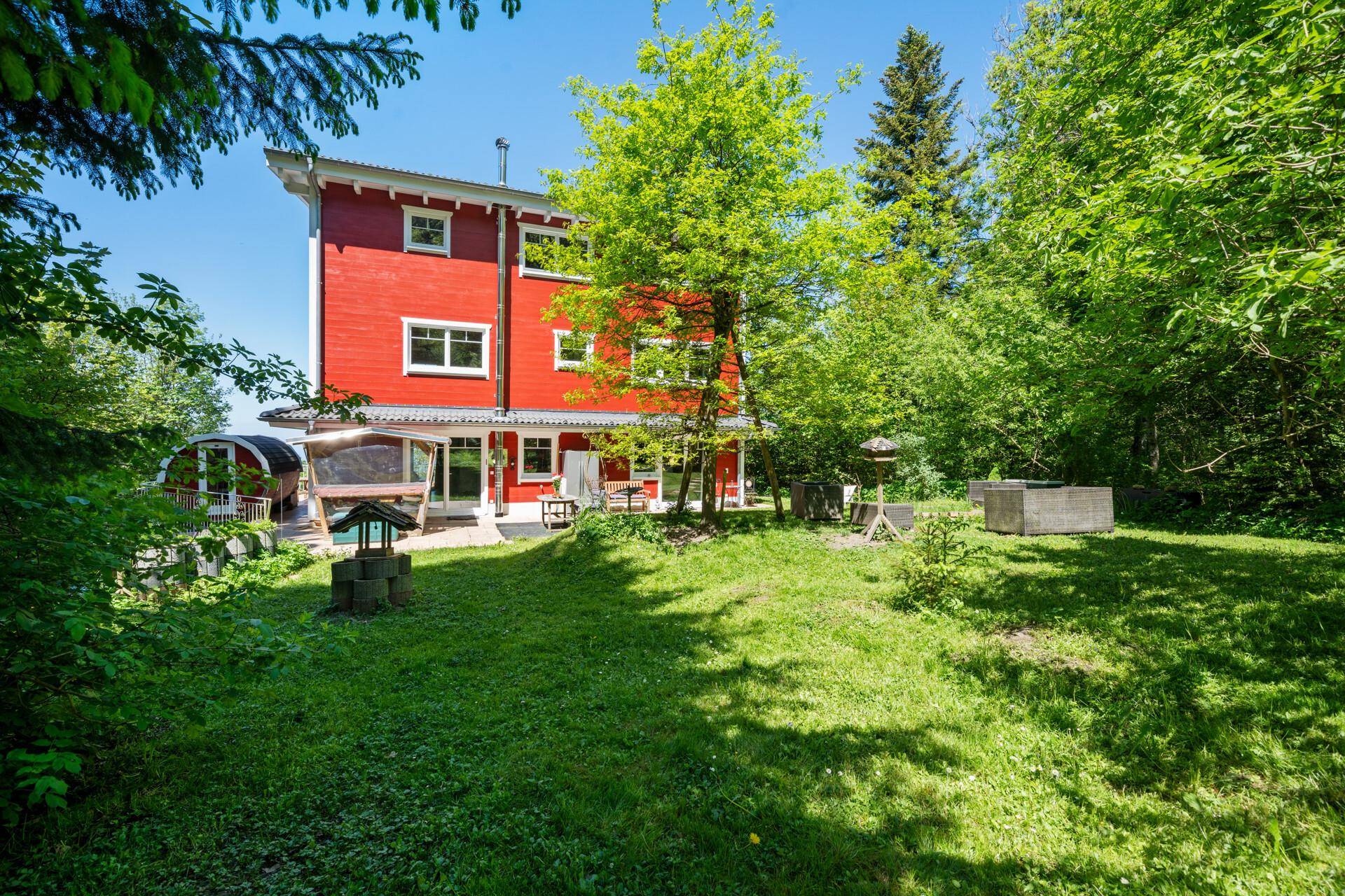 Großer, gepflegter Garten hinter dem roten Haus, umgeben von üppigem Grün.
