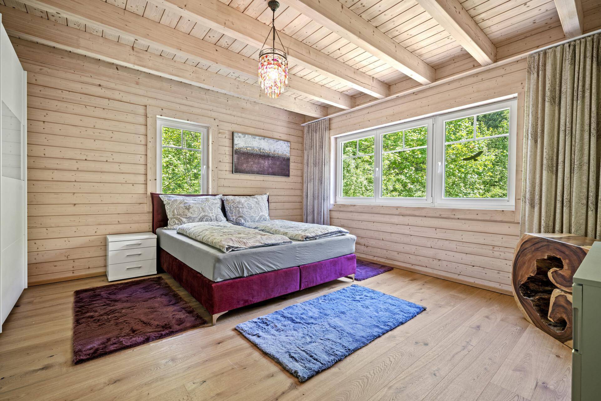 Gemütliches Schlafzimmer mit Doppelbett, Holzboden und großen Fenstern mit Blick ins Grüne.
