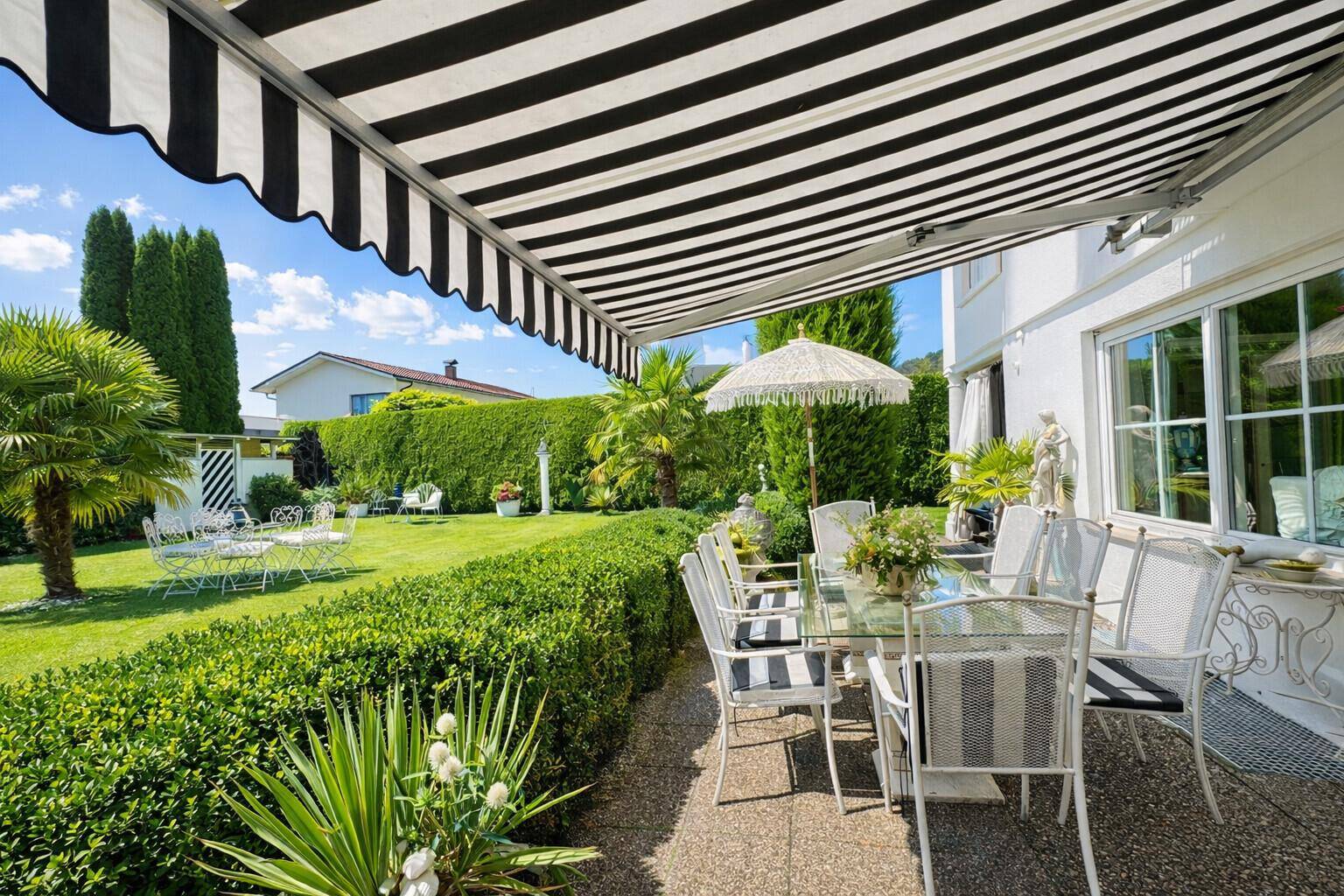 Geräumige Terrasse mit Essbereich unter einer Markise und weitem Blick in den Garten.