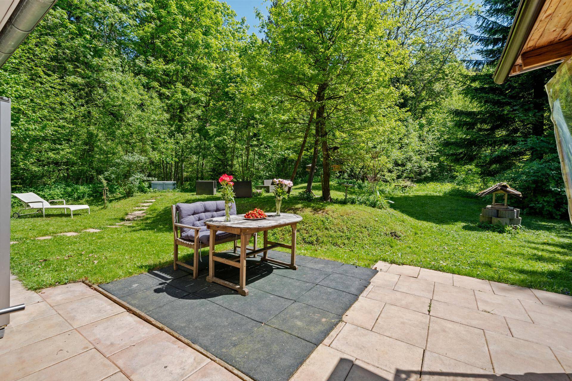 Gemütlicher Sitzbereich im Garten auf einer gepflasterten Terrasse, umgeben von Natur.