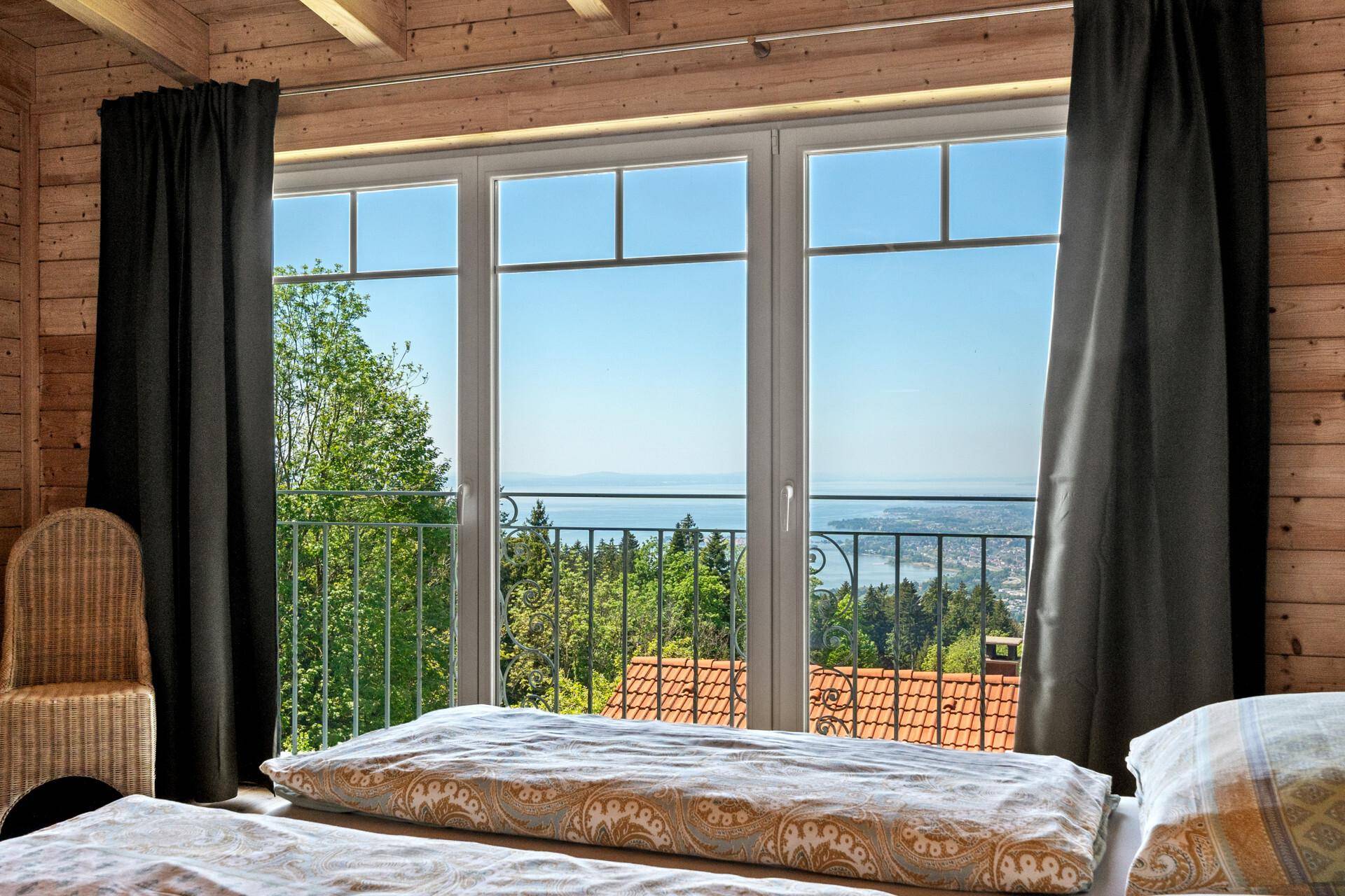 Helles Schlafzimmer mit Doppelbett, Holzboden und Panoramafenstern mit Seeblick.