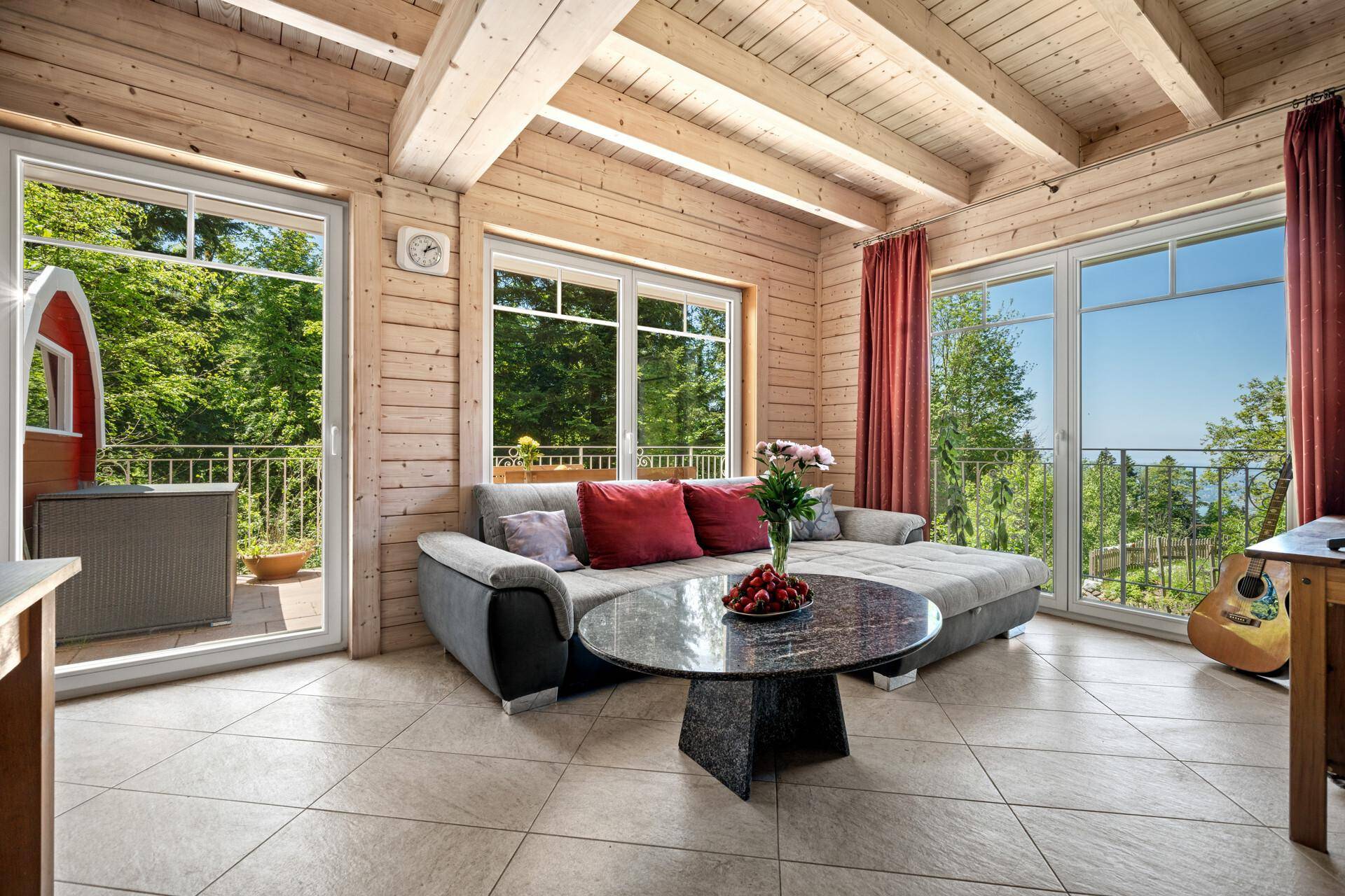 Heller Wohnbereich mit Holzwänden, Fliesenboden und großen Fenstern mit Waldblick.