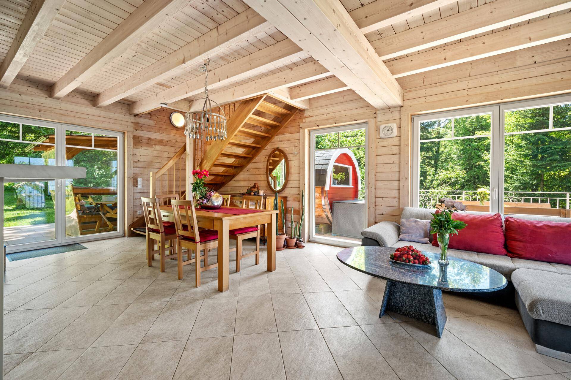 Offener Wohn- und Essbereich mit Holzbalkendecke, Fliesenboden und Zugang zur Terrasse.