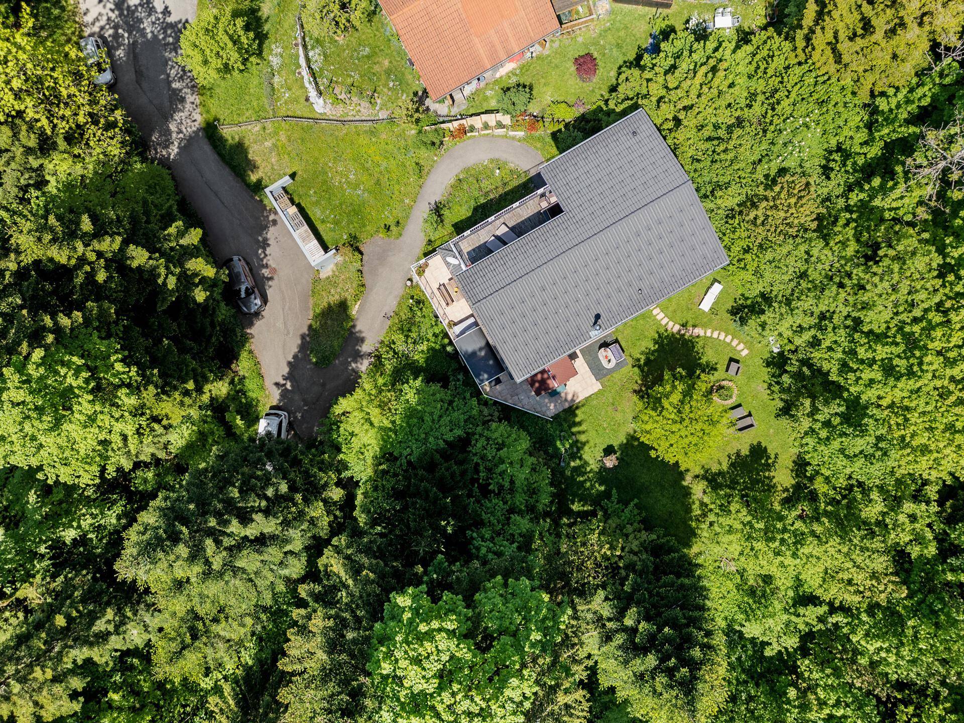 Draufsicht auf das Anwesen mit rotem Haus, Garten und Zufahrt, umgeben von Bäumen.