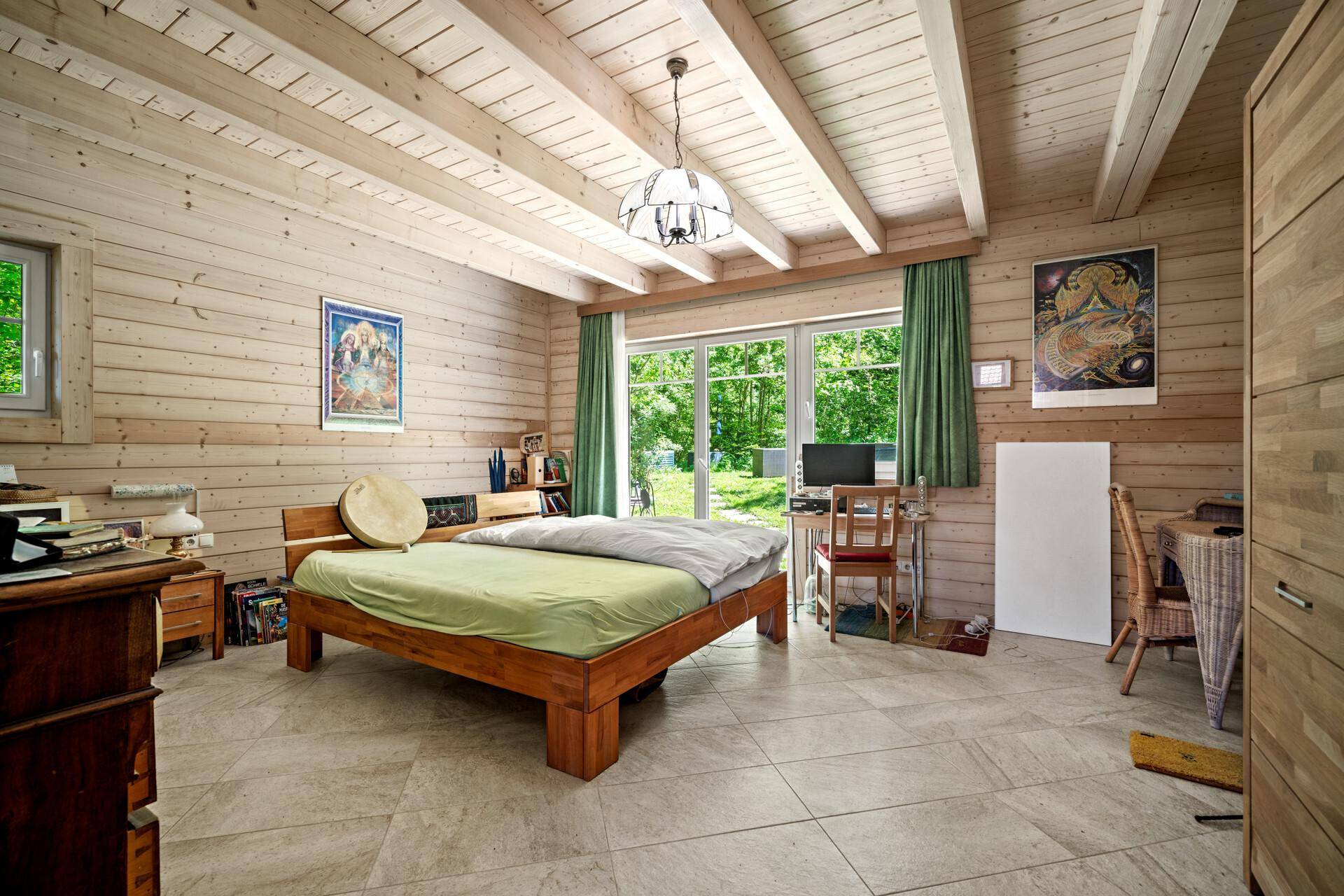 Gemütliches Schlafzimmer mit Holzwänden, Fliesenboden und großen Fenstern mit Blick ins Grüne.