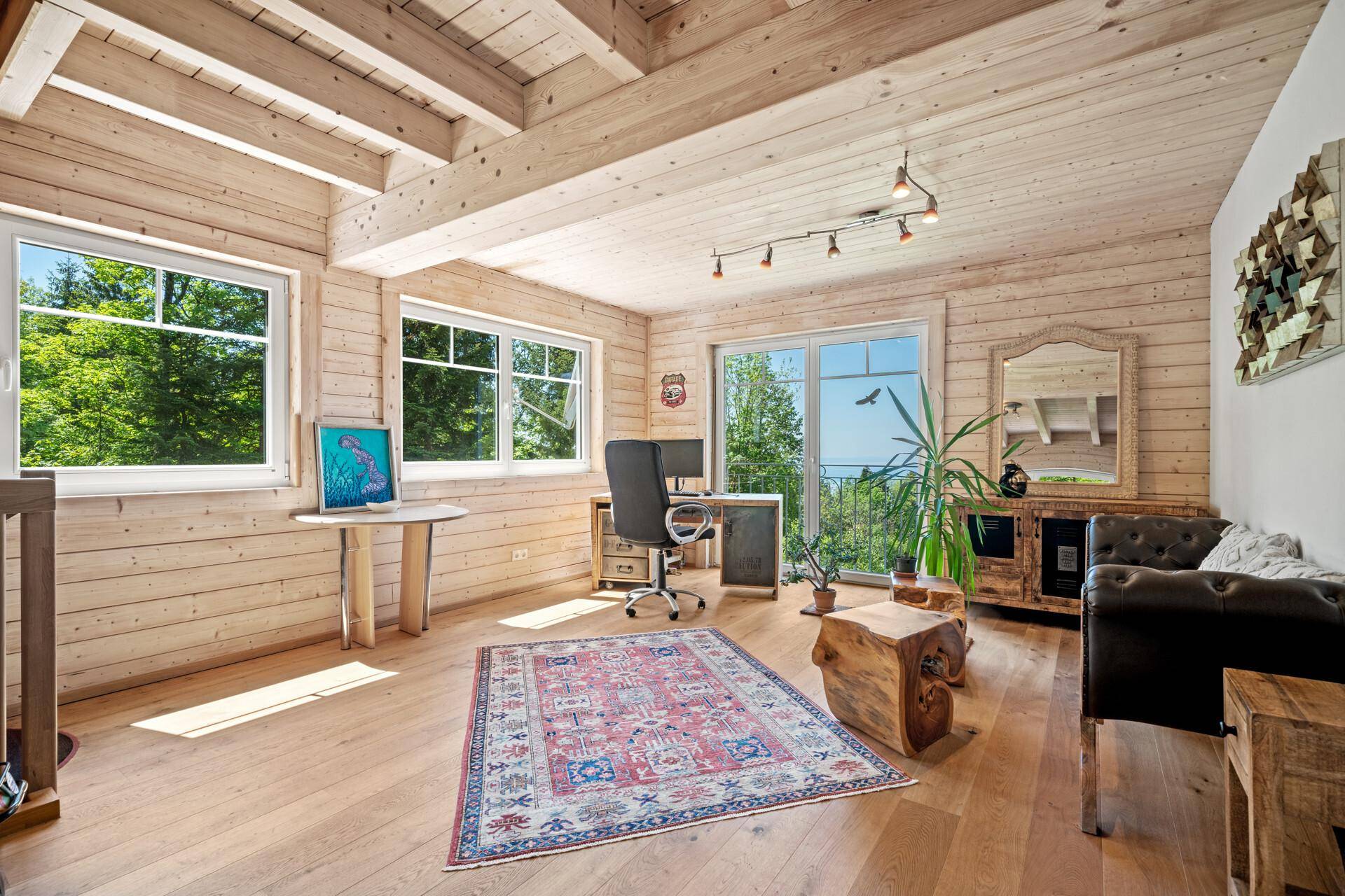 Heller Wohnraum mit Holzboden, Holzwänden und großen Fenstern mit Ausblick.