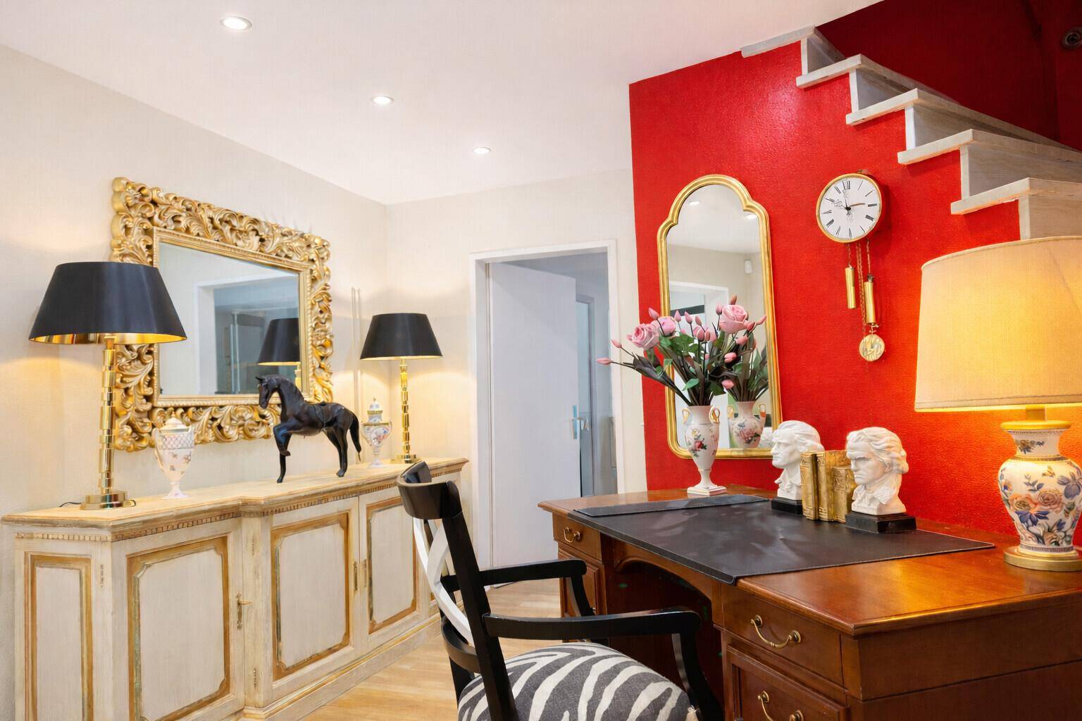 Arbeitszimmer mit roter Akzentwand, klassischem Schreibtisch und eleganten Möbeln.