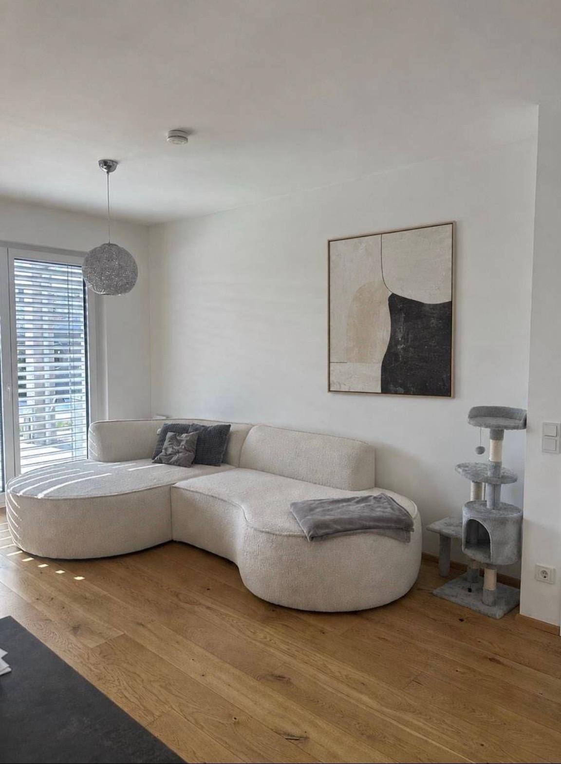 Gemütliches Wohnzimmer mit modernem, geschwungenem Sofa, Kunstwerk und Holzboden.