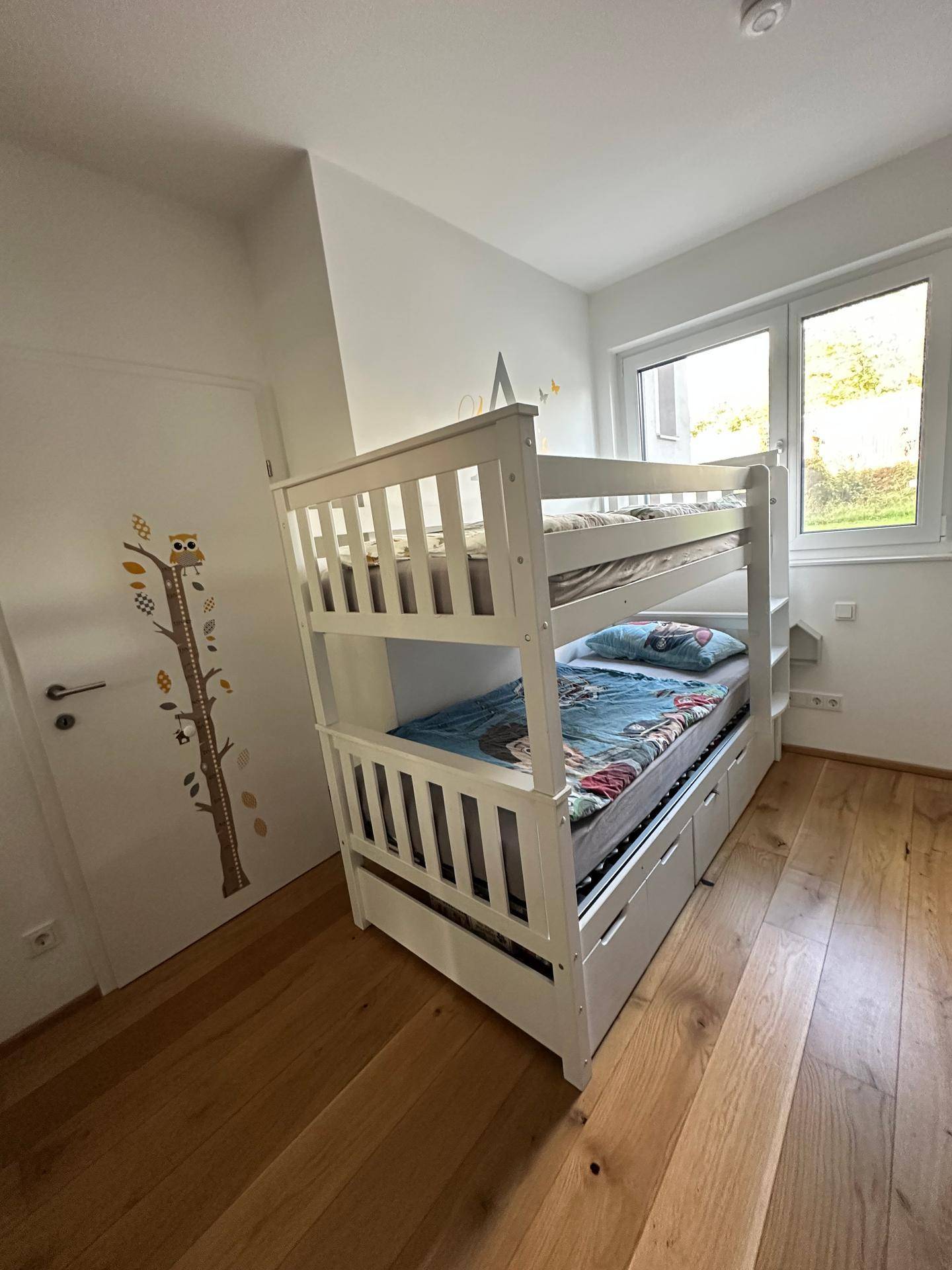 Kinderzimmer mit weißem Etagenbett, Holzboden und Fenster für natürliches Licht.