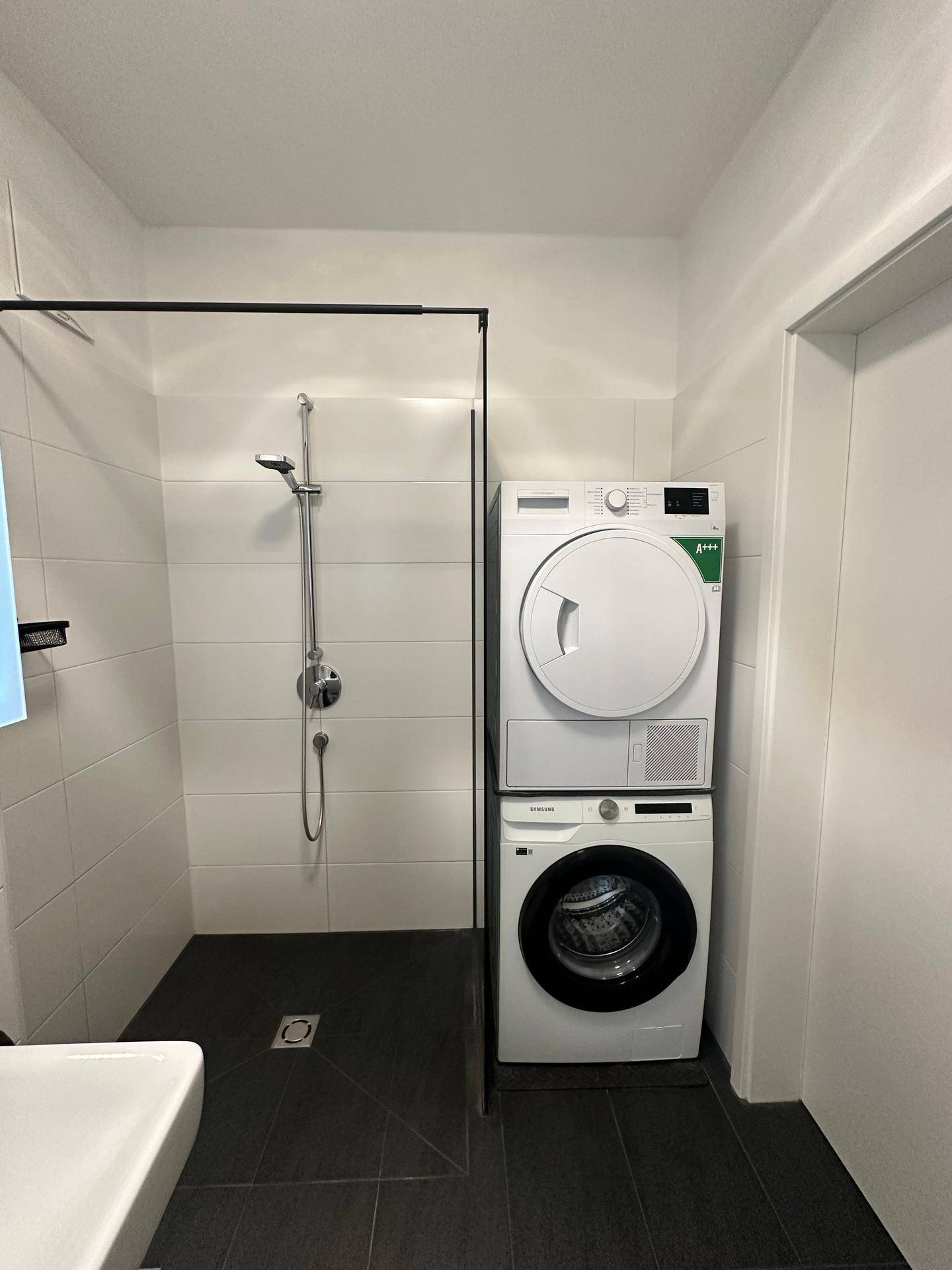 Modernes Badezimmer mit ebenerdiger Dusche und praktischem Waschmaschinen-Trockner-Turm.