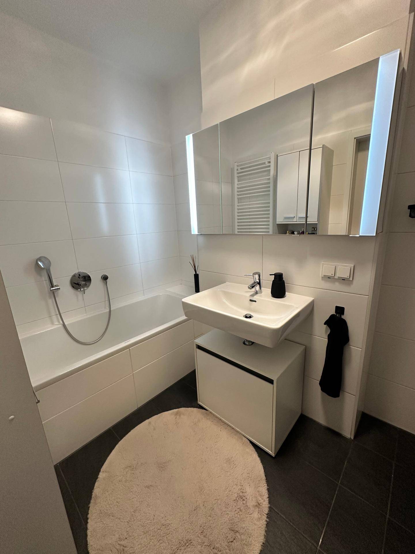 Helles Badezimmer mit Badewanne, Einzelwaschbecken und Spiegelschrank.