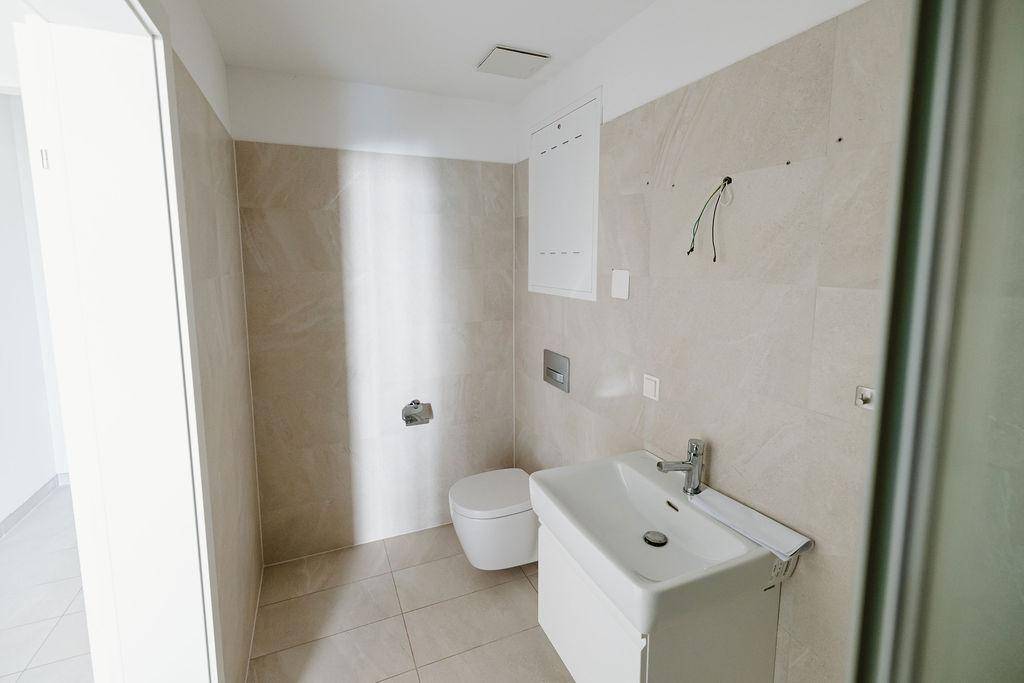 Zeitgemäßes Badezimmer mit wandhängendem WC, Waschbecken und hellen Fliesen.