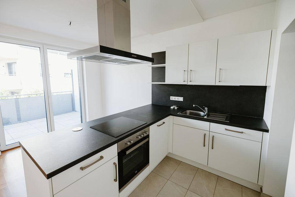 Funktionale Einbauküche mit Spüle, Kochfeld und direktem Zugang zum sonnigen Balkon.