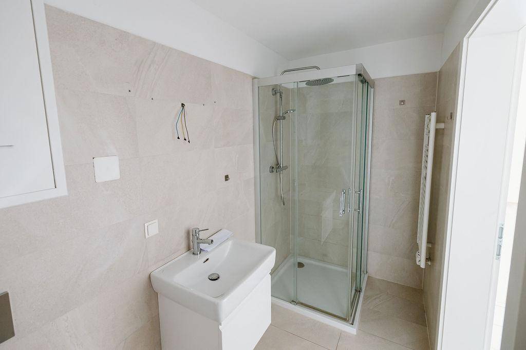 Modernes Badezimmer mit beigefarbenen Fliesen, Duschkabine und beheiztem Handtuchhalter.