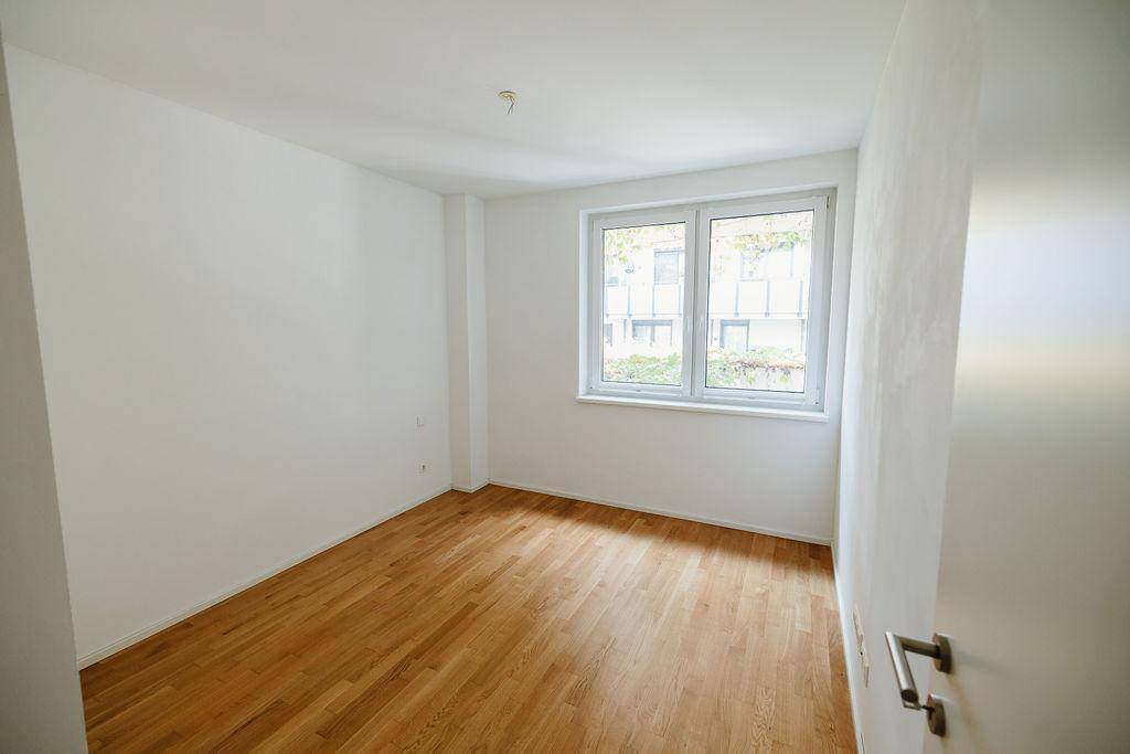 Helles Schlafzimmer mit Parkettboden und großem Fenster, bereit zur individuellen Gestaltung.
