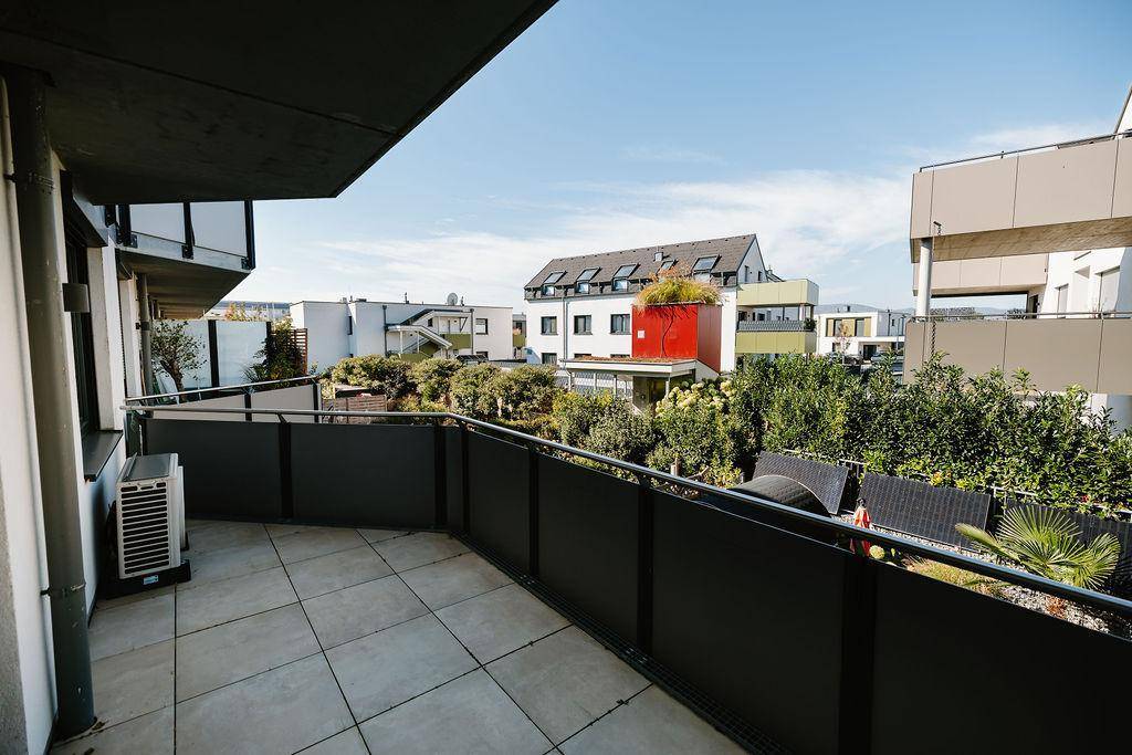 Geräumiger Balkon mit Fliesenboden und Blick auf die umliegenden Wohngebäude und viel Grün.