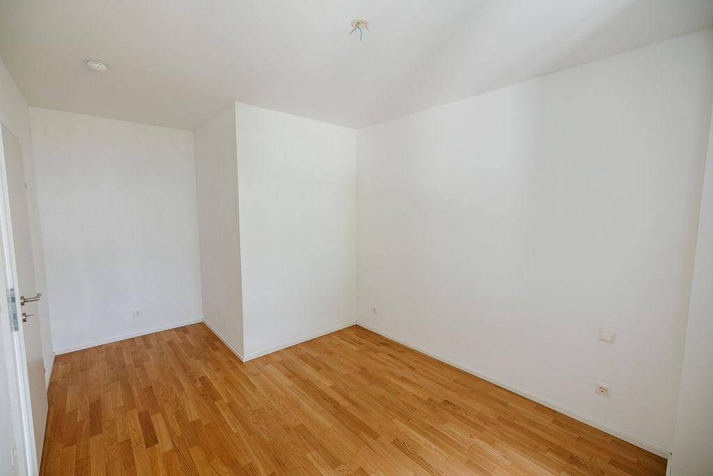 Geräumiges Schlafzimmer mit hellem Parkettboden und weißen Wänden, ideal für Ruhe und Entspannung.