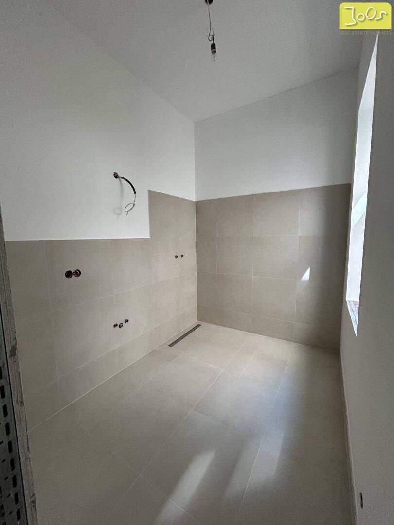 Unfertiges Badezimmer mit beigefarbenen Fliesen an Boden und Wänden, bereit für die Installation.