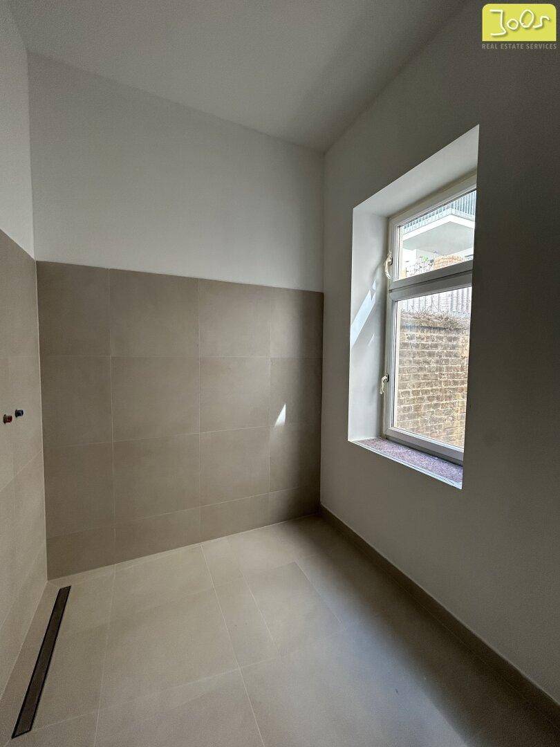 Unfertiges Badezimmer mit beigefarbenen Fliesen und einem Fenster für natürliche Belüftung.
