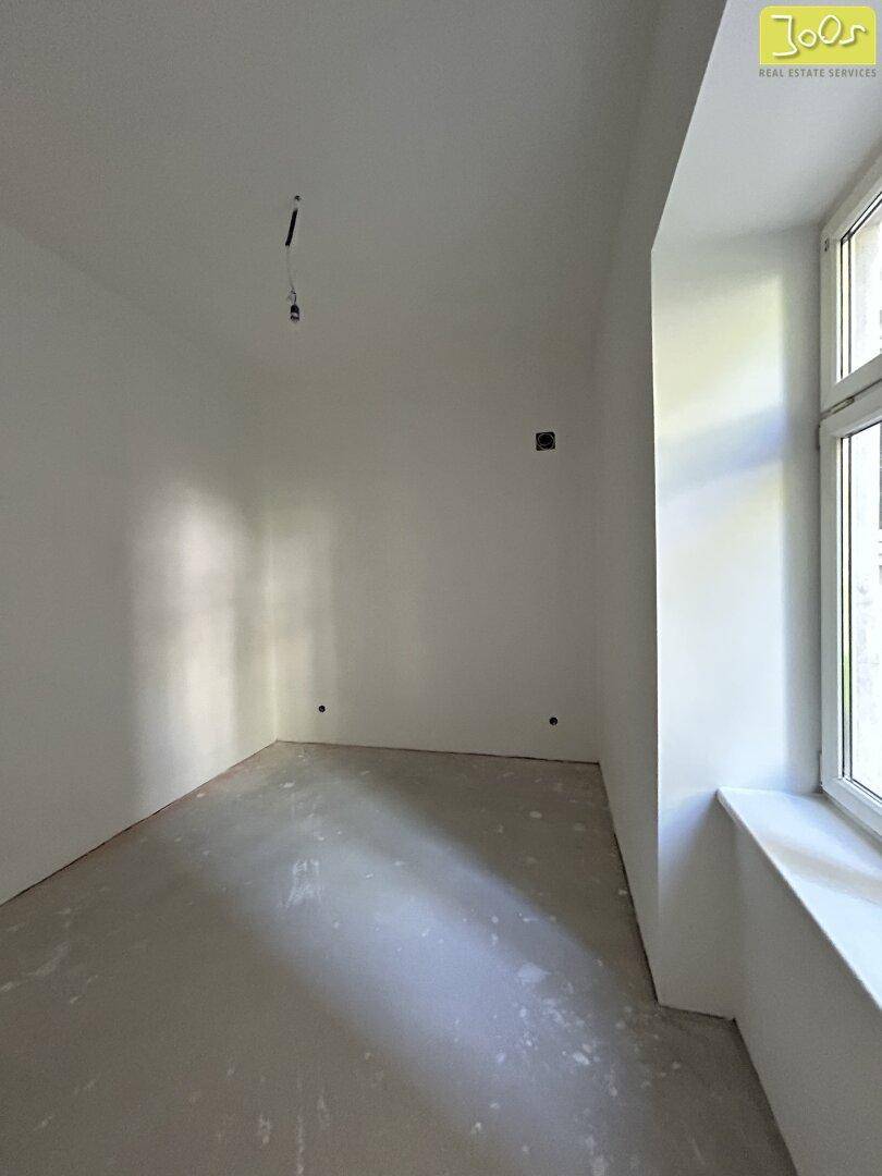Unmöblierter Raum mit einem großen Fenster, das viel Tageslicht hereinlässt, ideal für ein Schlafzimmer.