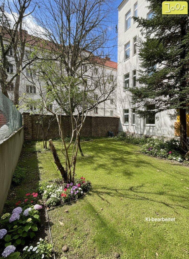 Grüner Gartenbereich mit blühenden Blumenbeeten und Rasenfläche hinter dem Gebäude.