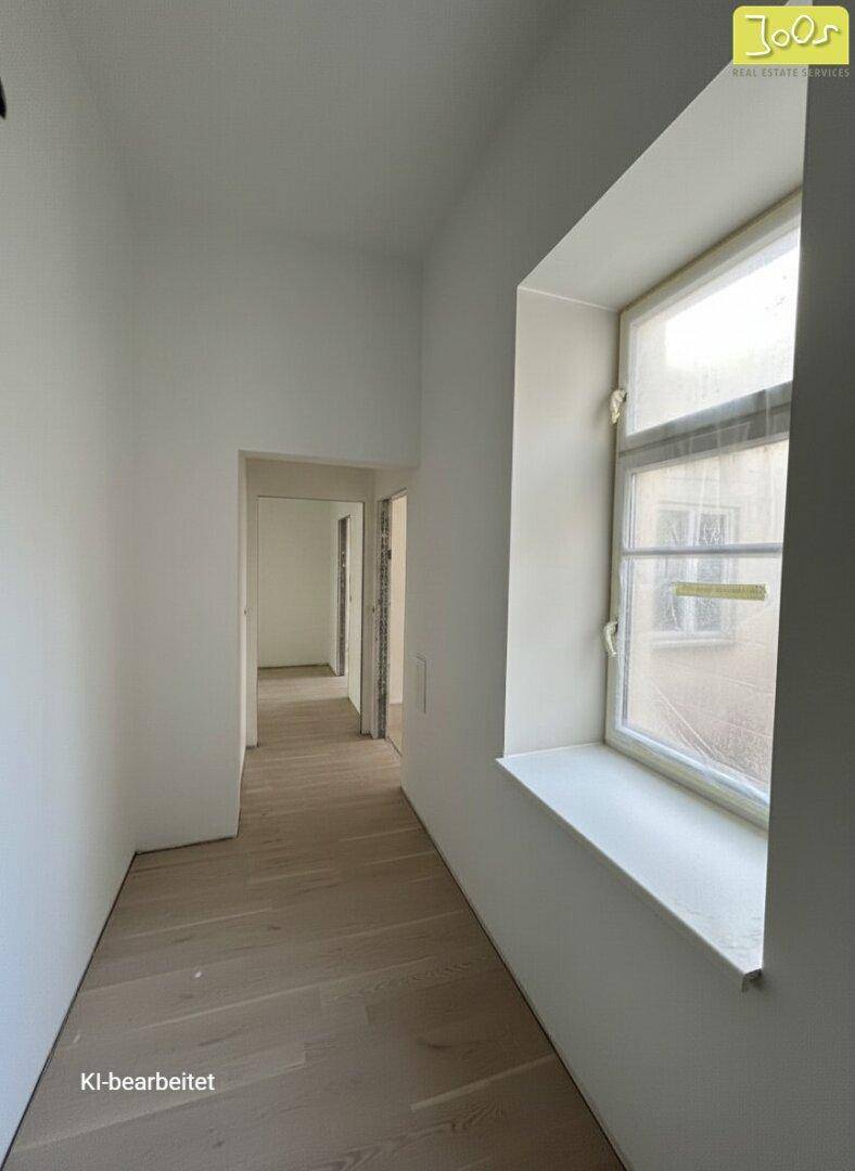 Heller Flur mit hellem Holzfußboden und einem Fenster, das Tageslicht hereinlässt.