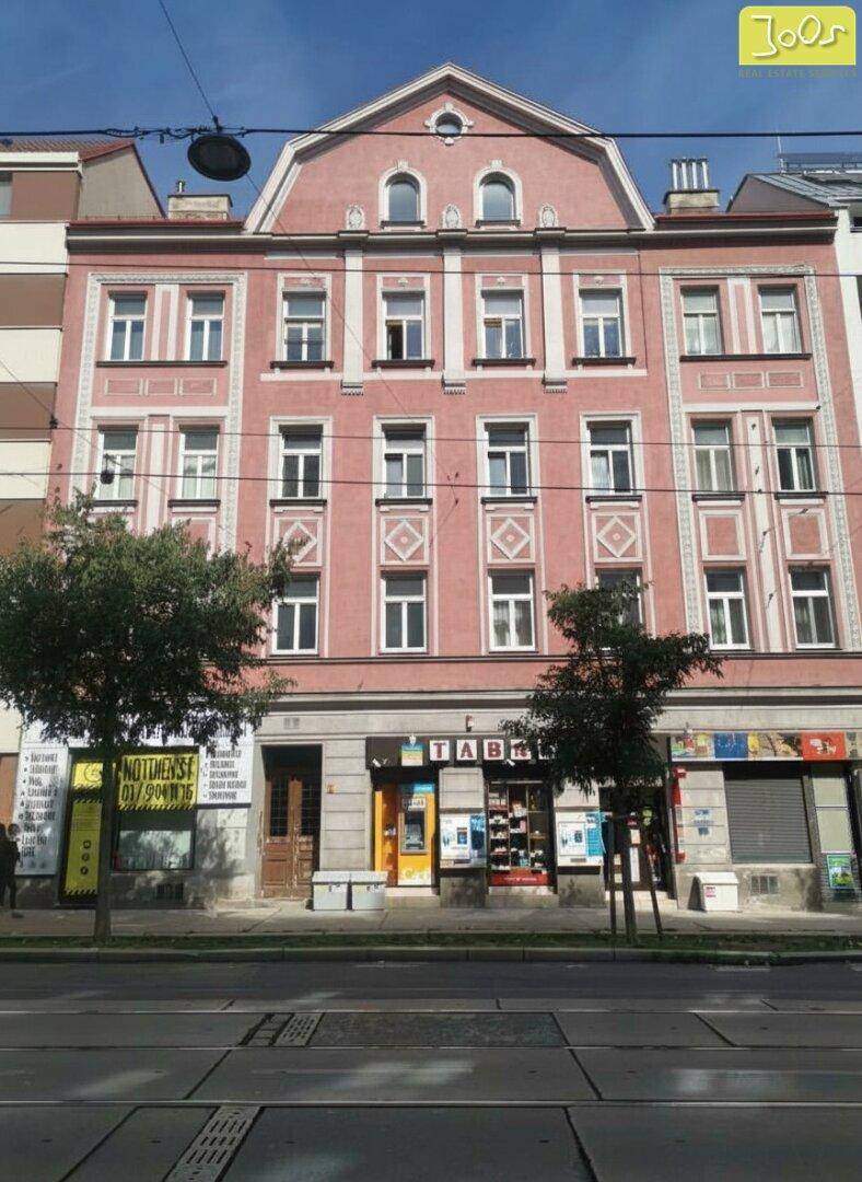 Historische rosa Fassade eines Altbaus mit Geschäften im Erdgeschoss an einer belebten Straße.