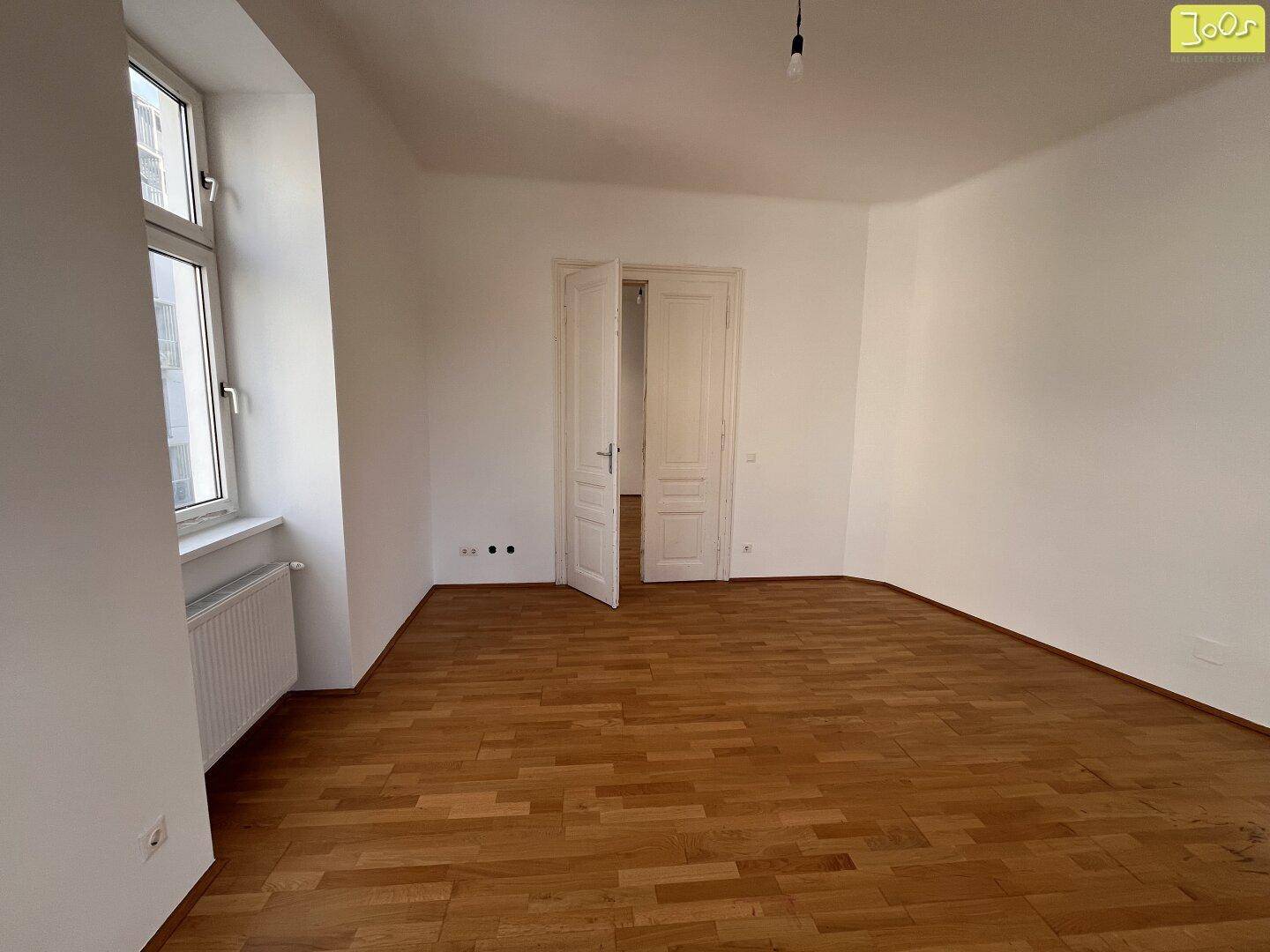 Leeres Zimmer mit Parkettboden und einer Doppeltür, bereit für neue Bewohner.