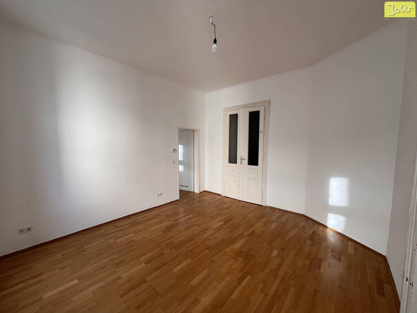 Geräumiges Zimmer mit Parkettboden und einer Doppeltür, ideal für Wohn- oder Schlafbereich.