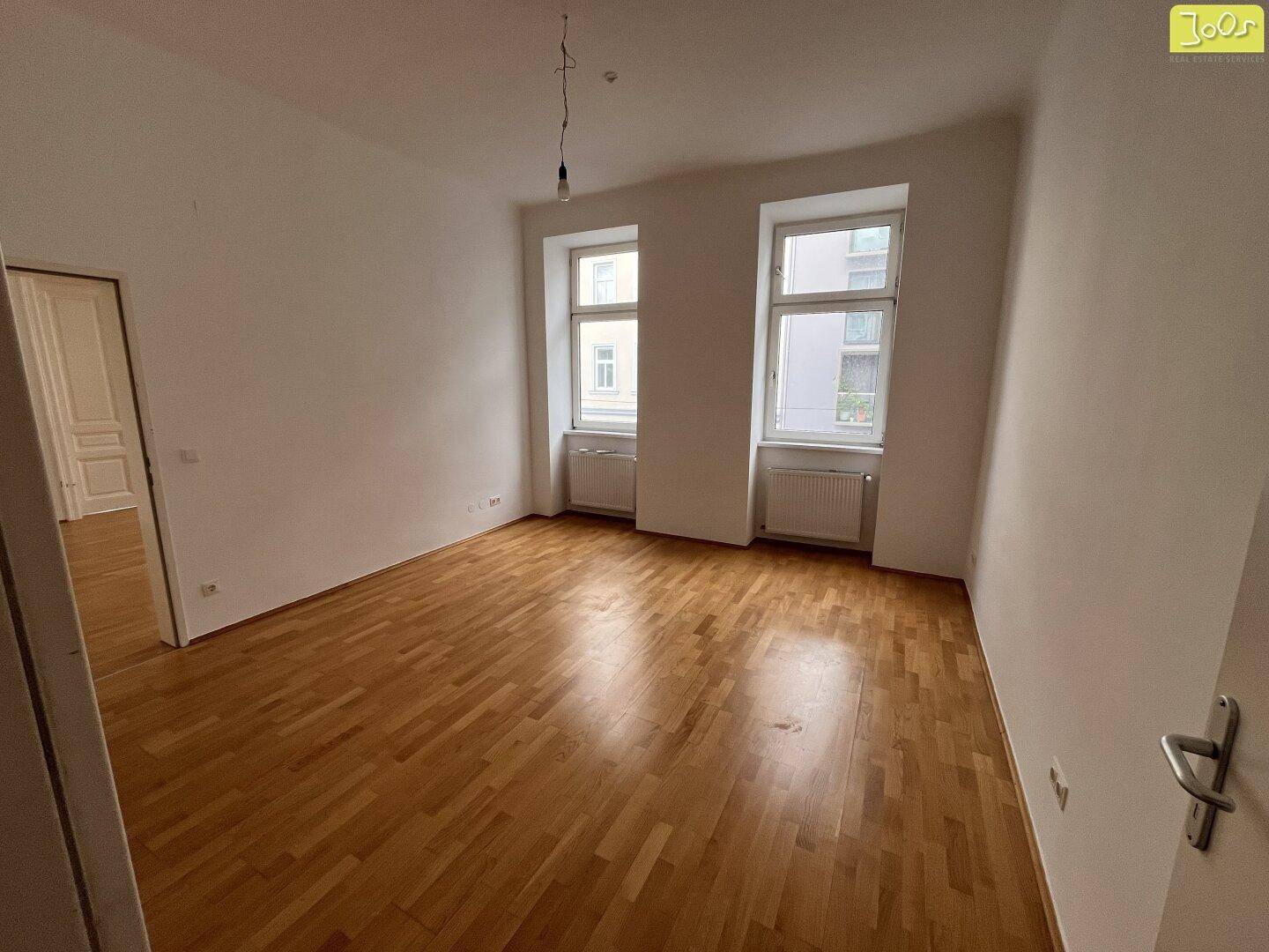 Helles Zimmer mit Holzboden und zwei Fenstern, bietet viel Tageslicht und Raum.