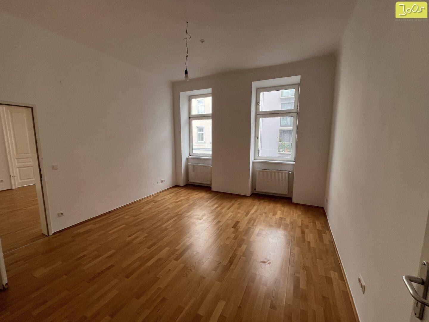 Lichtdurchflutetes Zimmer mit Parkettboden und zwei Fenstern, bietet eine angenehme Atmosphäre.